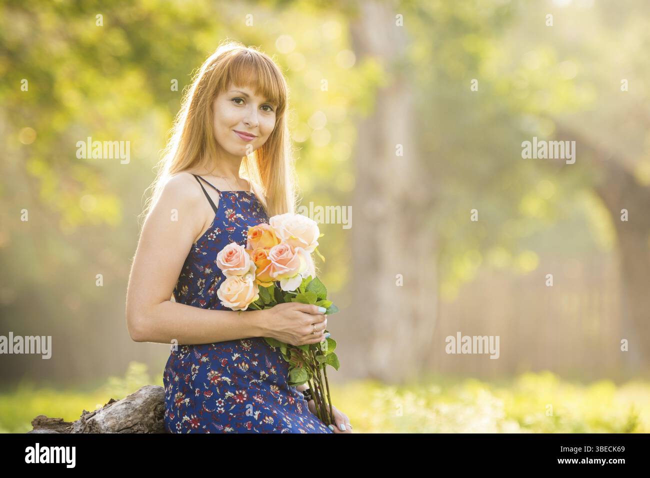Schöne junge Frau mit einem Strauß Rosen in den Händen auf dem Hintergrund einer grünen sonnigen verschwommen Stockfoto