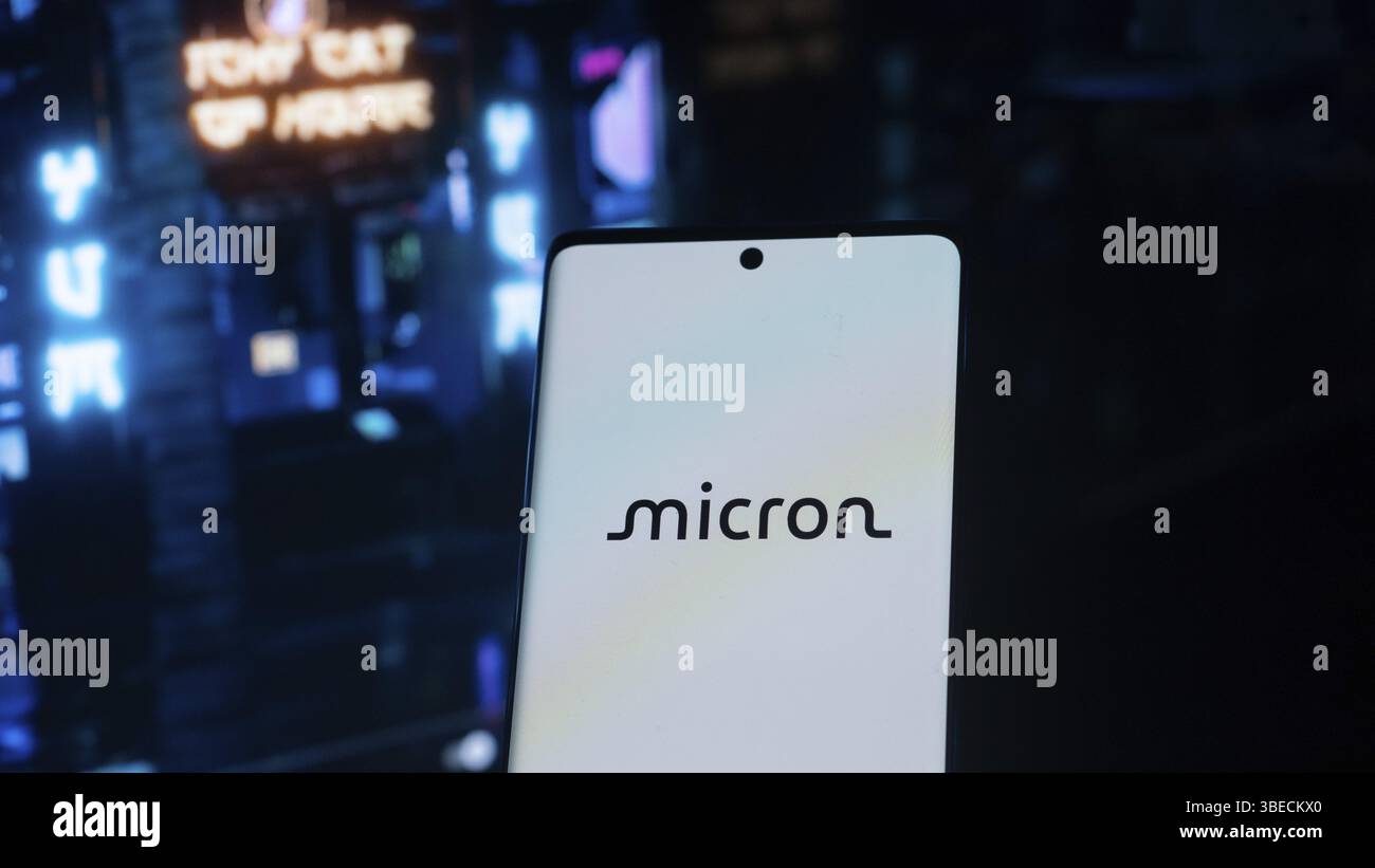 Mikrometer-Logo auf einem Telefon vor einem neonbeleuchteten dunklen Hintergrund, futuristischer Vibe Stockfoto