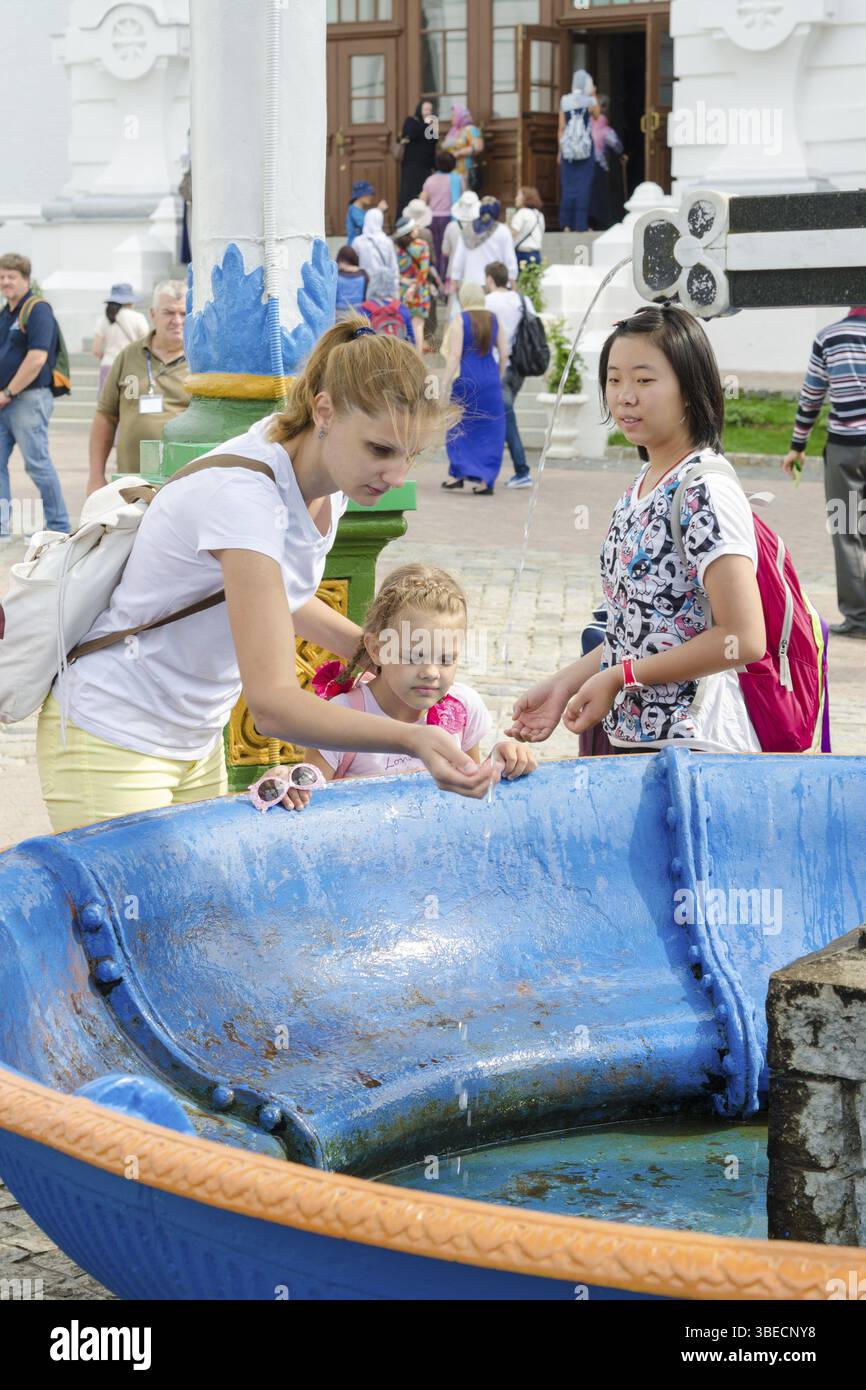 Sergiev Posad - 10. August 2015: Sie Besucherin der Heiligen Dreifaltigkeit St. Sergius Lavra wäscht das Gesicht des Babys mit heiligem Wasser am Baldachin über der Tasse mit einem c Stockfoto