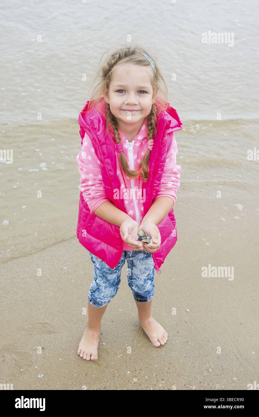 Drei Jahre altes Mädchen stehend mit Muscheln in der Hand, die am Strand zu sammeln Stockfoto