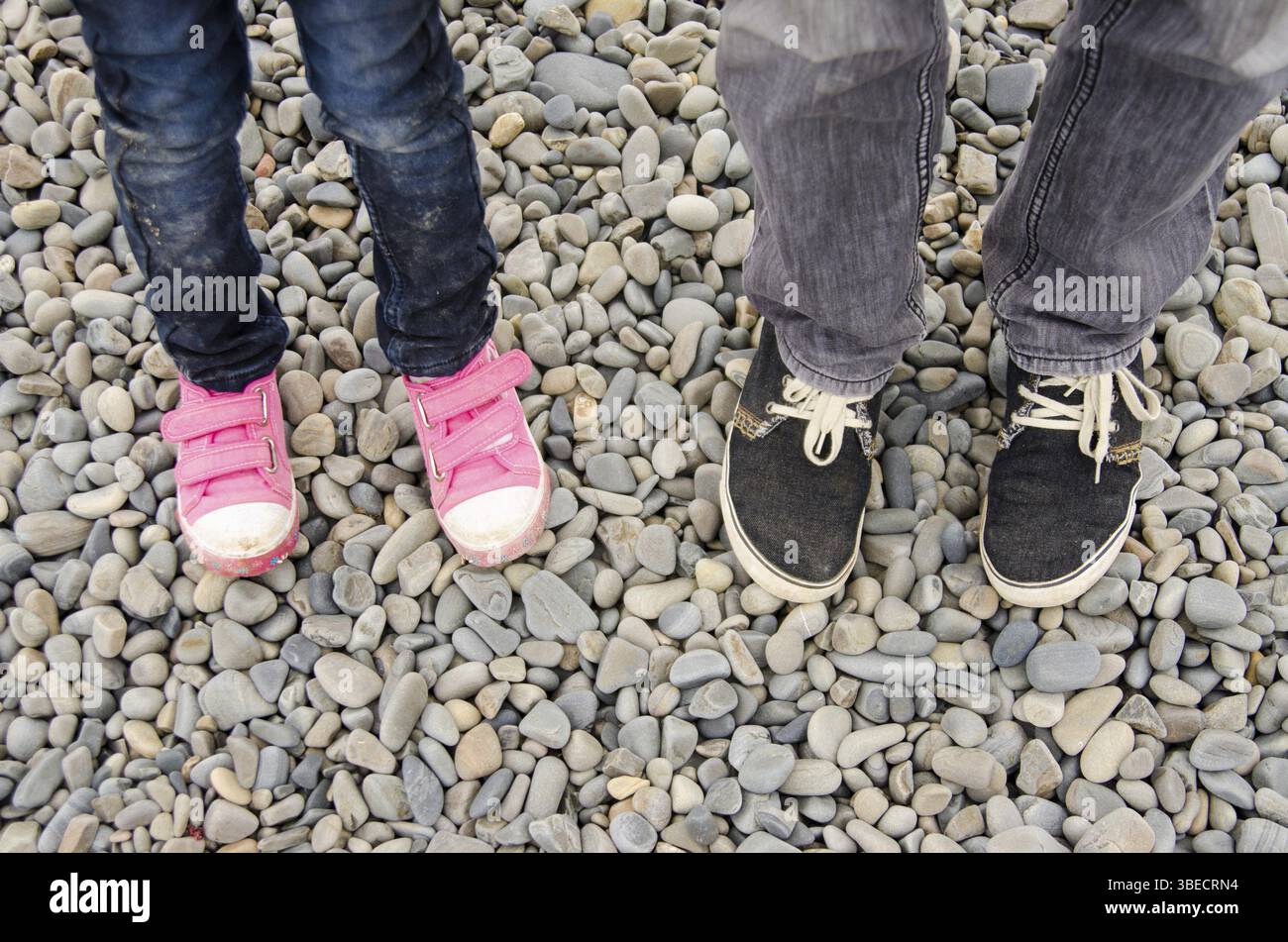 Zwei Paar Füße in Sneakers, Erwachsene und Kinder, sind auf dem Kies Stockfoto