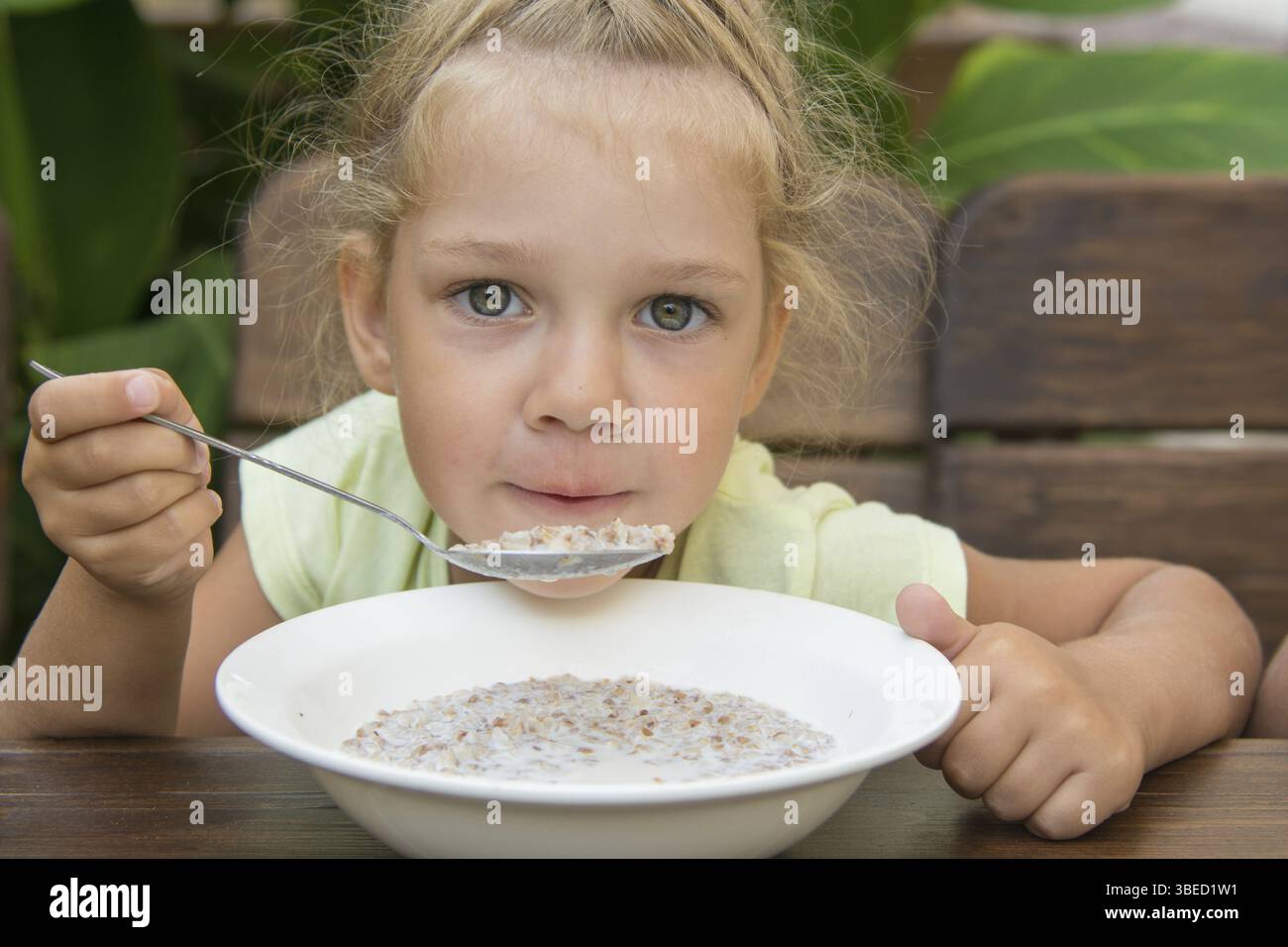 Vier-Jahres-Mädchen am Tisch an der frischen Luft weht auf einen Löffel Brei Stockfoto