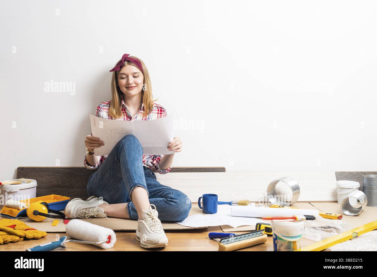 Innenarchitektin studiert Renovierungsprojekt. Lächelndes hübsches Mädchen, das auf dem Boden sitzt, mit Papiermuster. Renovierung und Inneneinrichtung des Hauses. Stockfoto