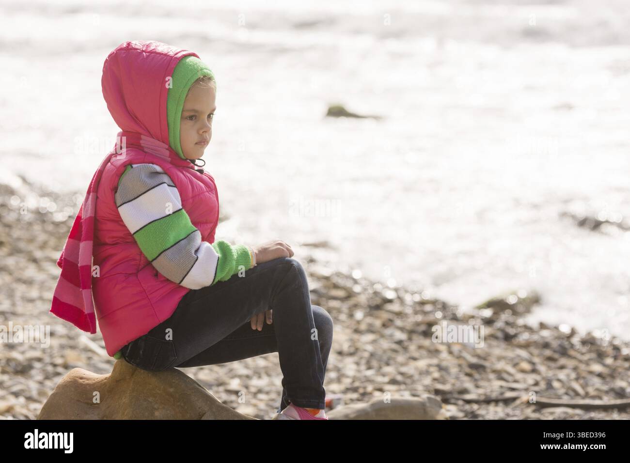 Nachdenklich Mädchen sitzen auf einem Felsen auf den steinigen Strand auf das Meer und die Blicke in die Ferne Stockfoto