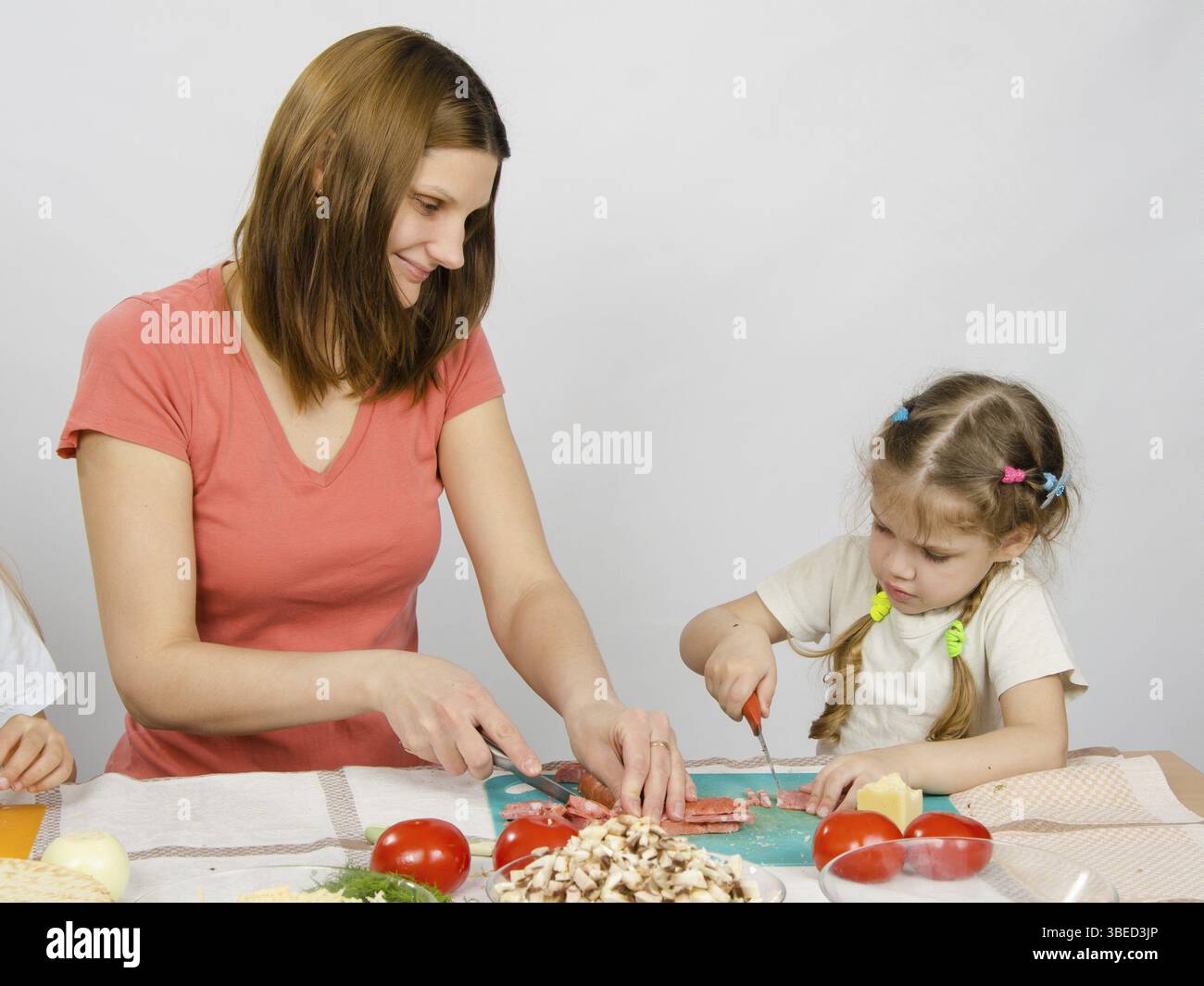 Mutter lehrt Tochter zu einem sechs-Jahres-Schnitt mit einem Messer Produkte zum Kochen am Küchentisch Stockfoto