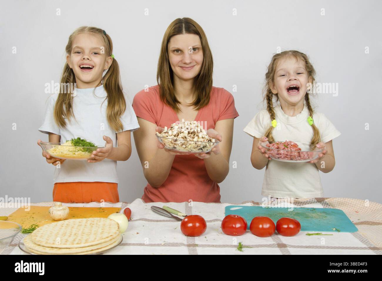 Mutter mit zwei Töchtern glücklich Halteplatte mit in Scheiben geschnittenen Produkten für pizza Stockfoto