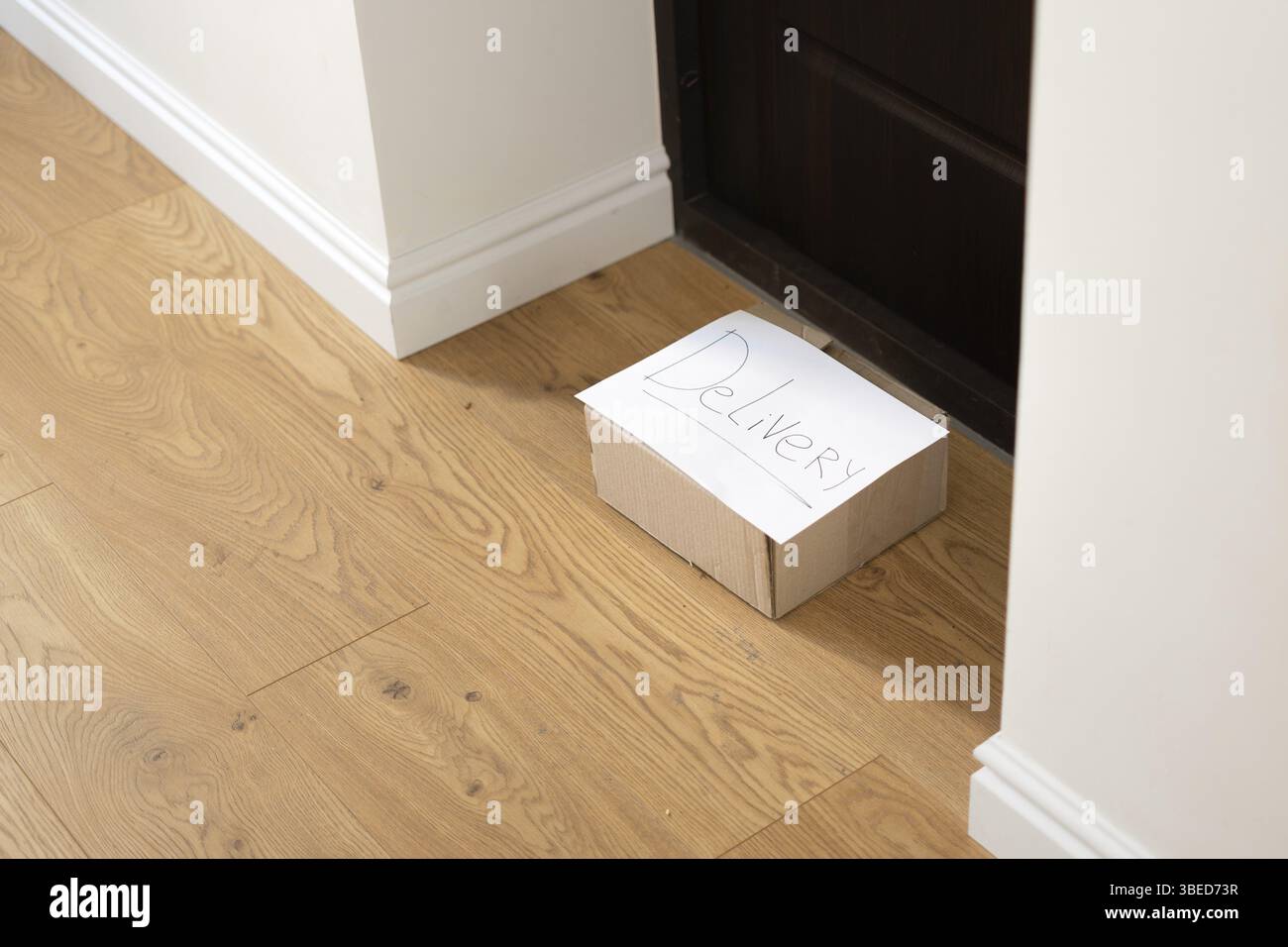 Junge Frau zu Hause in Handschuhen und Maske, die die Lieferbox vom Boden nimmt. Kontaktloses Lieferkonzept. COVID-19-Sicherheit Stockfoto