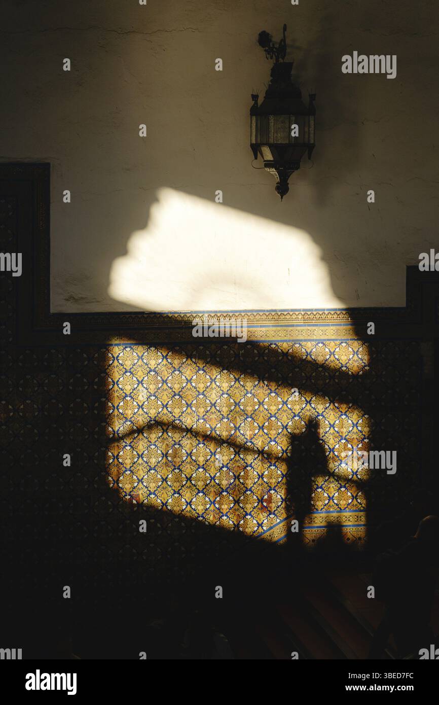 Sevilla, Spanien - 15. Dezember 2024 Schattensilhouette auf gemusterter Wand mit Vintage-Lampe und geometrischem Fliesendesign. Spanien Platz, Plaza de Espana Stockfoto