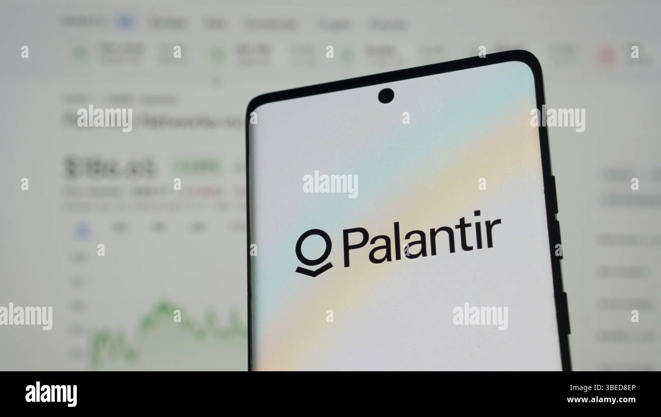 Palantir-Logo auf Smartphone mit verschwommenen Finanzdaten im Hintergrund Stockfoto