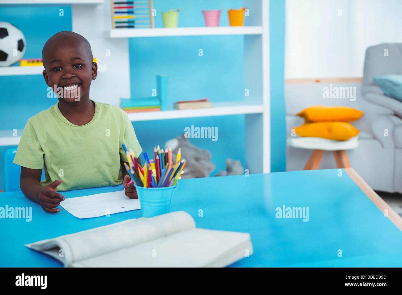 Afroamerikanischer Junge auf Papier am blauen Tisch mit Buntstiften im Spielzimmer, Kopierraum Stockfoto