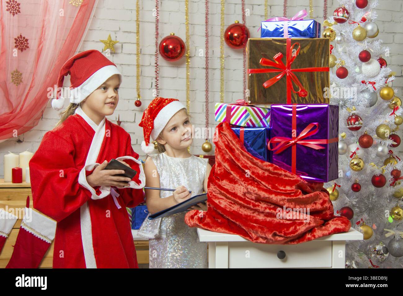 Zwei Mädchen Schwestern, vier und sechs Jahren in das neue Jahr Kostüme sind an der Tasche mit Weihnachtsgeschenken Stockfoto