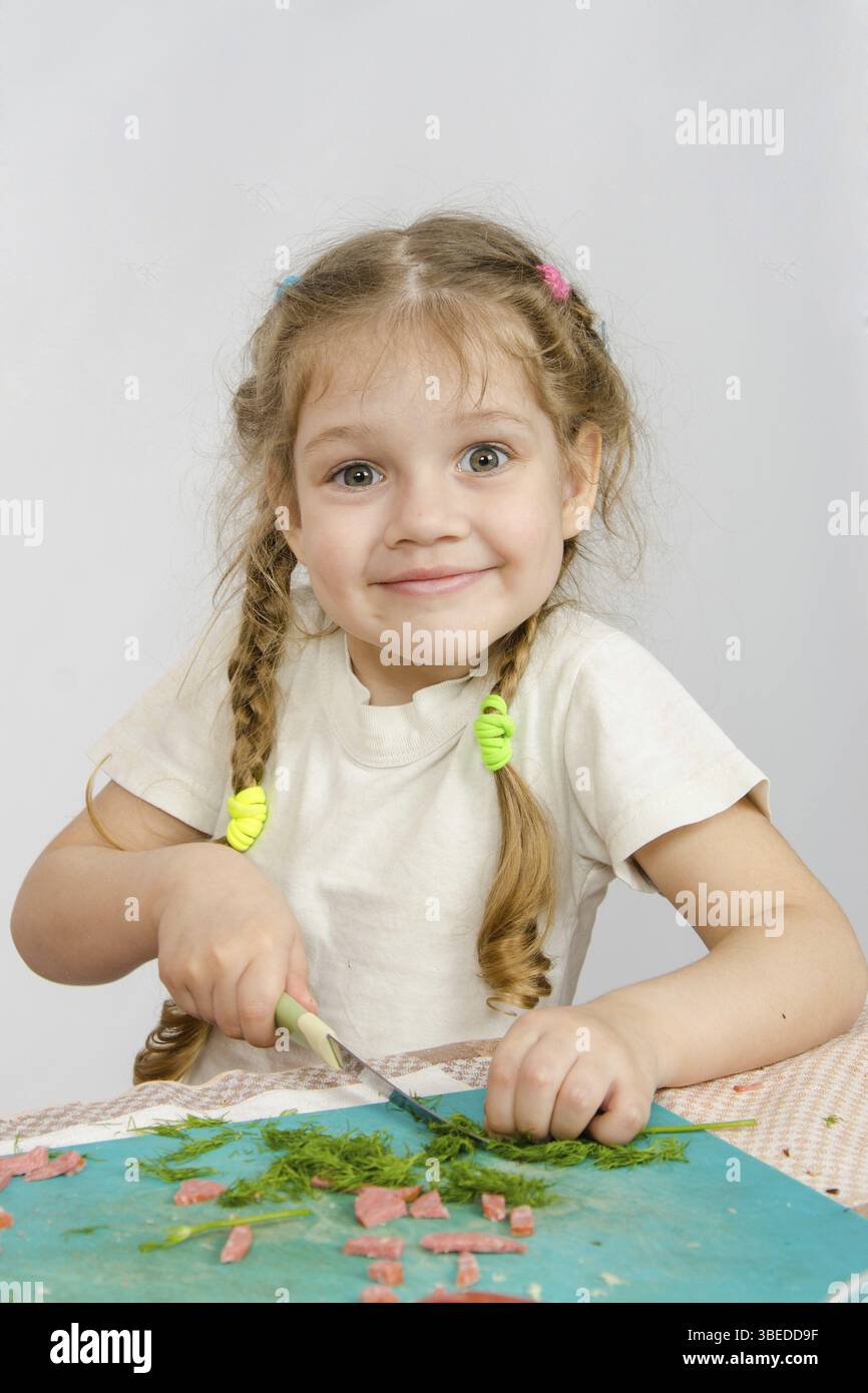 Sechs Jahre alten Mädchen, die versuchen, um die Grüns am Küchentisch schneiden Stockfoto