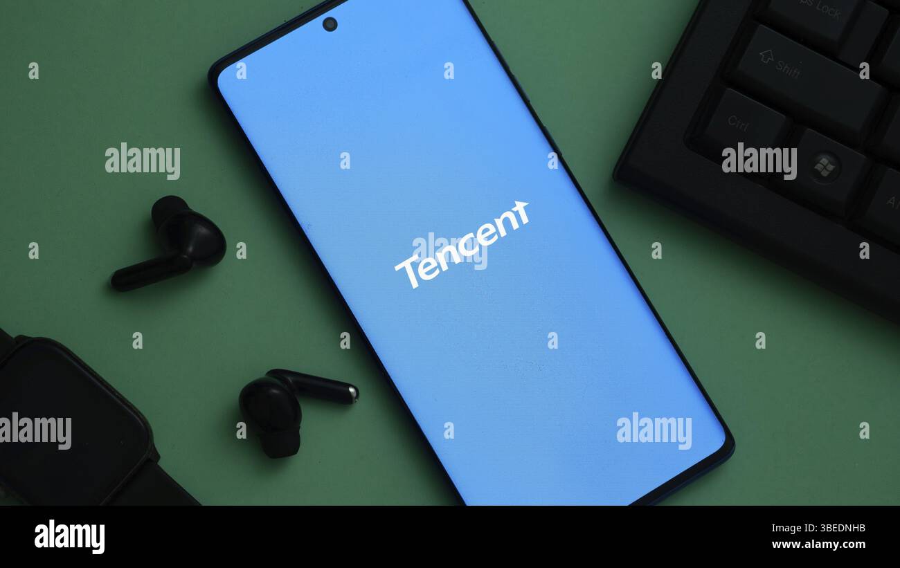 Tencent-Logo auf einem Smartphone neben technischem Zubehör auf grüner Oberfläche Stockfoto
