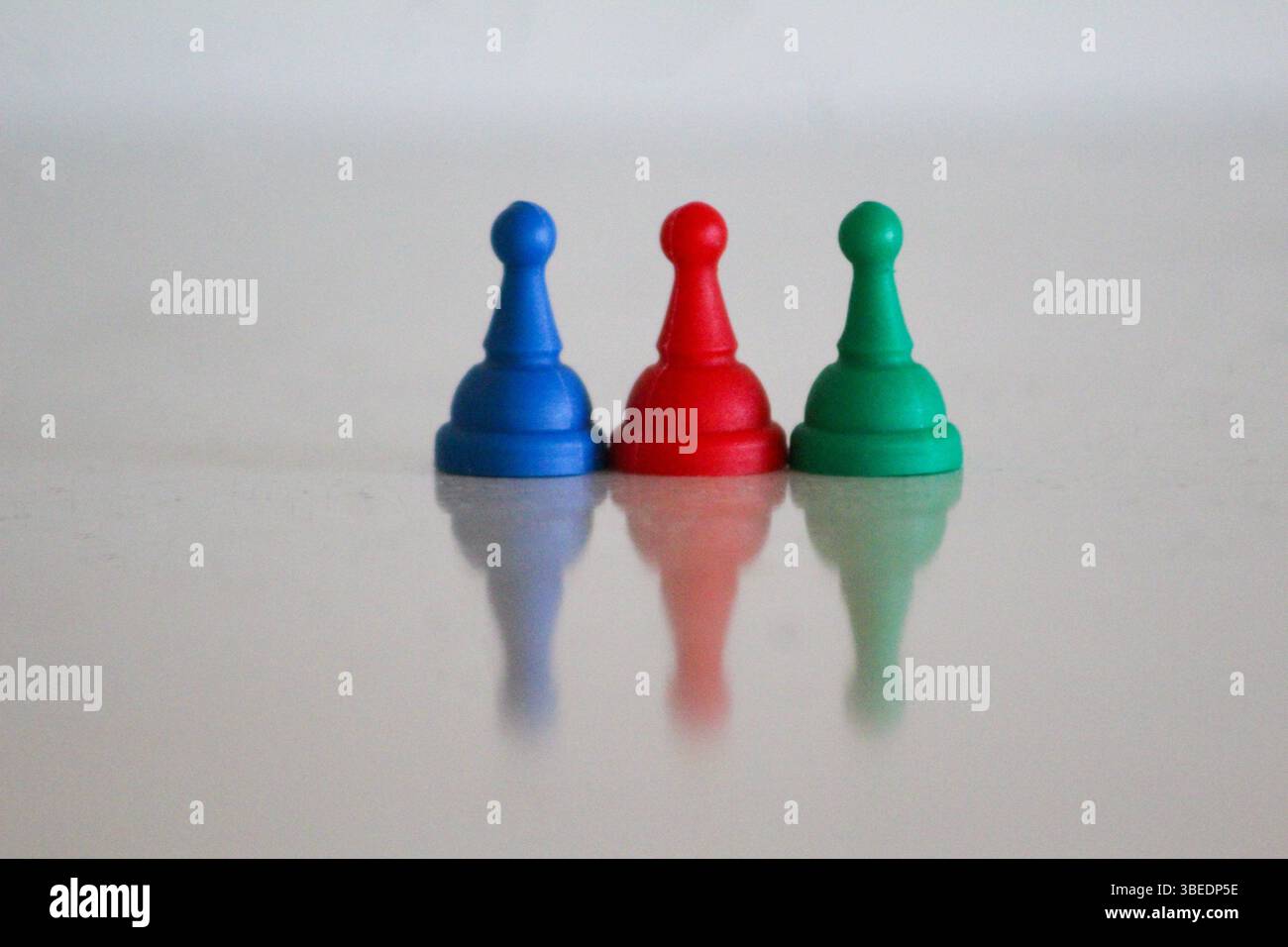 Drei Spielfiguren in Blau, Rot und Grün, symbolisch angeordnet, um die Farben der aserbaidschanischen Nationalflagge zu reflektieren, mit sanfter Reflexion. Stockfoto