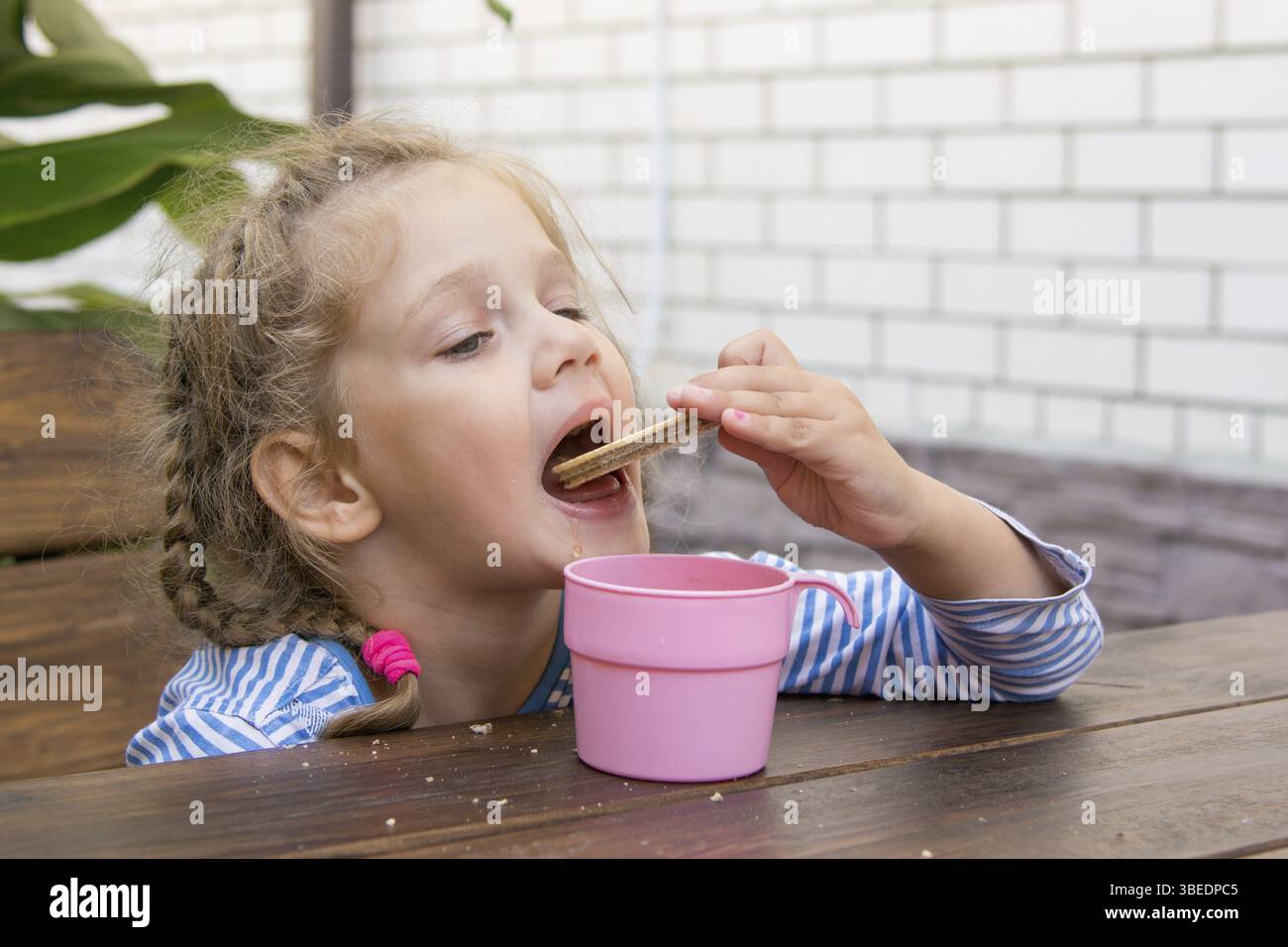 Vierjährige Mädchen Waffeln Essen und trinken Tee an einem Tisch auf der veranda Stockfoto