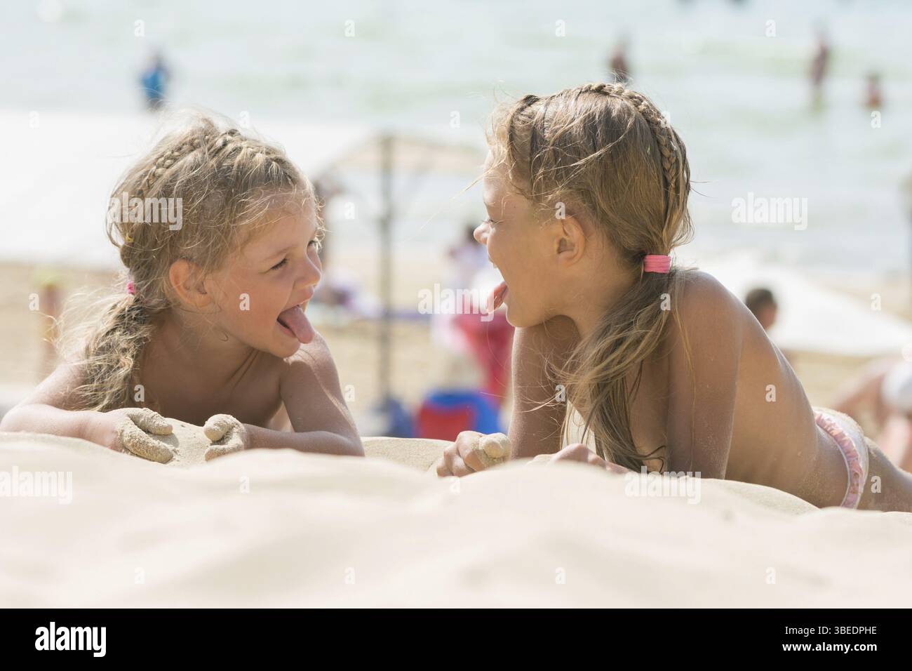 Zwei glückliche kleine Mädchen zeigen sich gegenseitig Zungen am Sandstrand Stockfoto