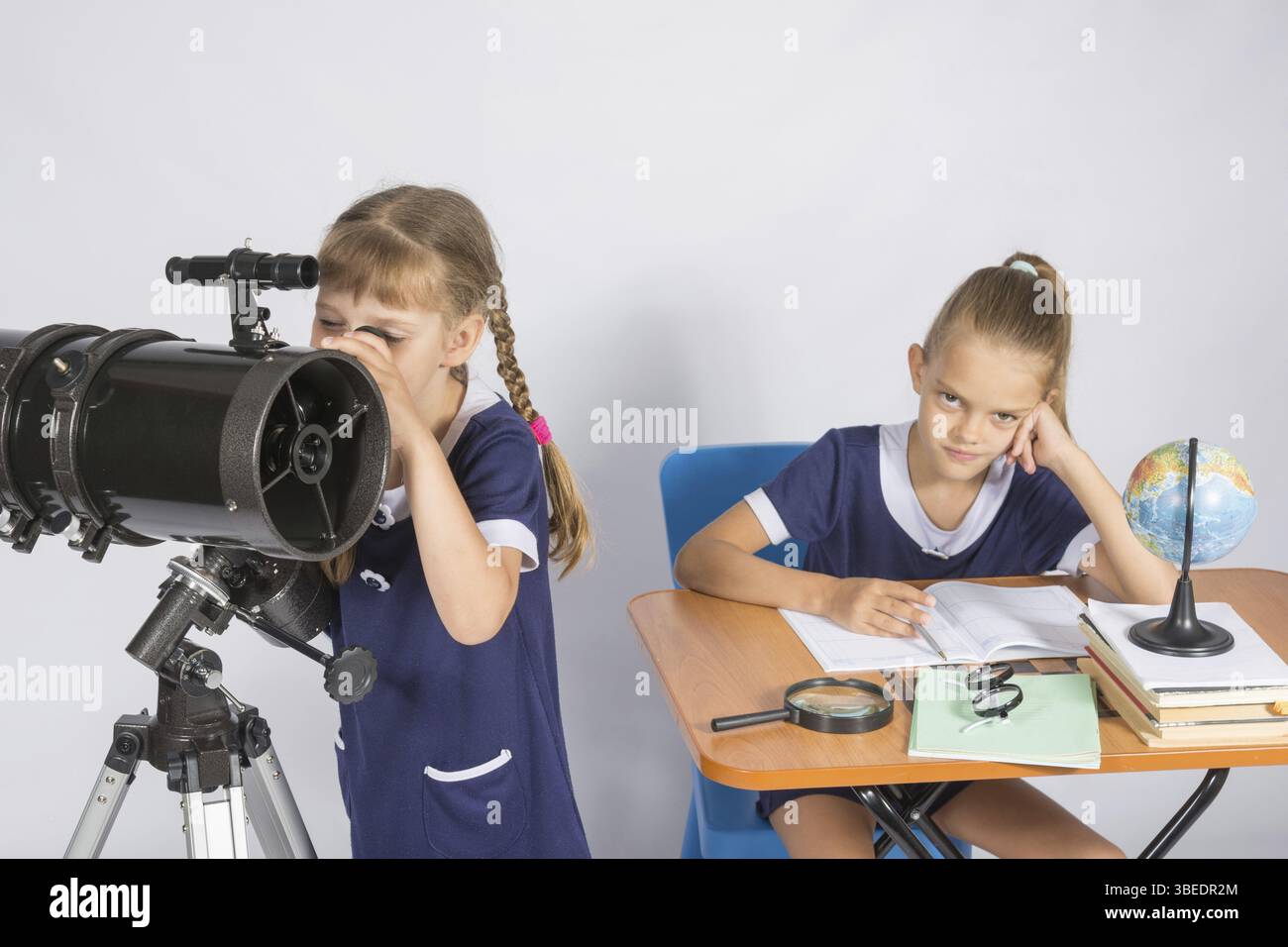 Mädchen-Astronom schaut zum Himmel durch ein Teleskop, das andere Mädchen sitzt am Tisch Stockfoto