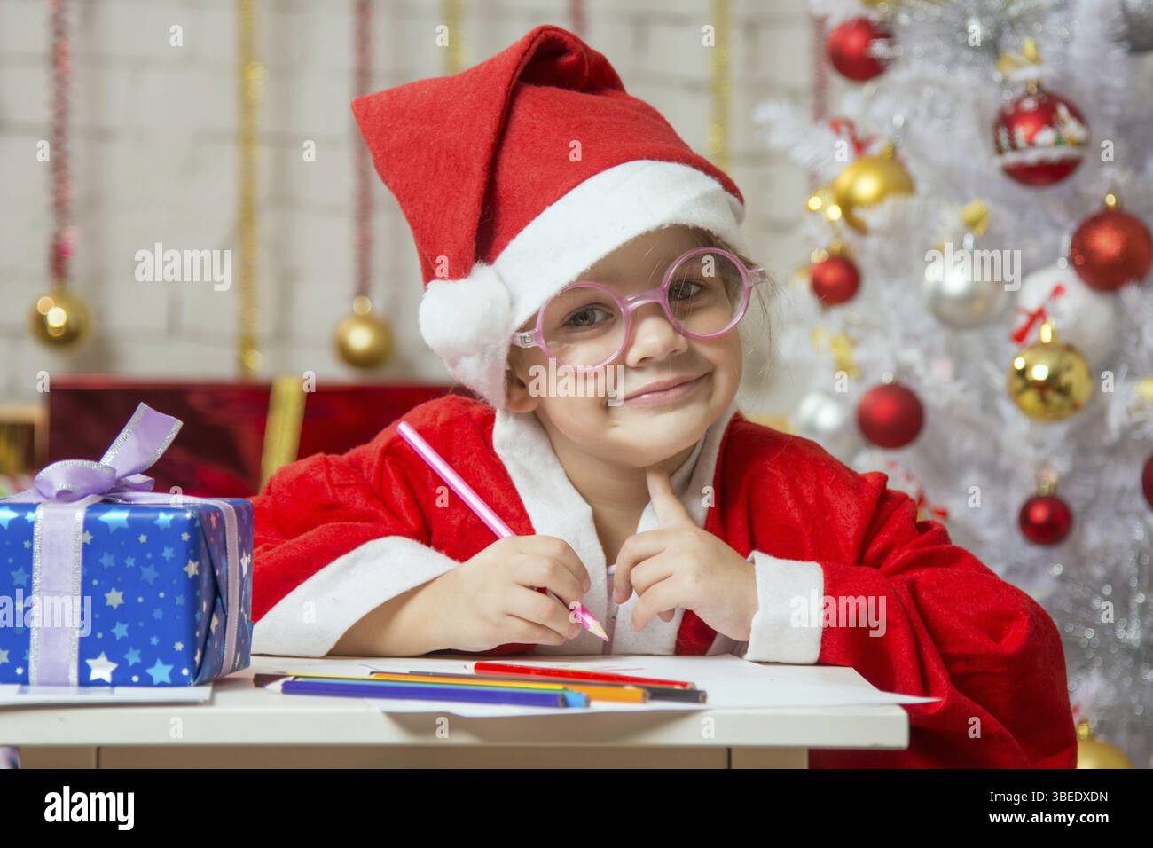 Vierjährige Mädchen gekleidet in einen roten Anzug Weihnachtsmann Ziehungen sind Bleistifte in eine festliche Weihnachten Innenausstattung Stockfoto