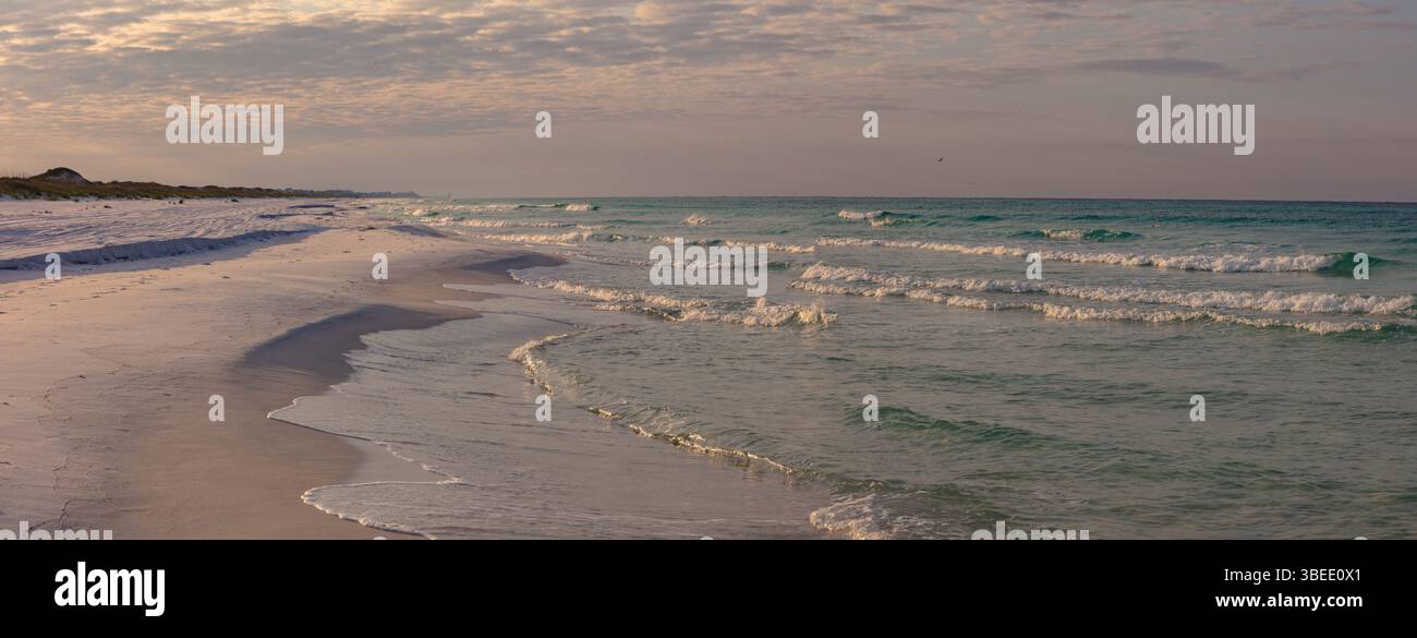 Sanfte Wellen Rollen in den wunderschönen weißen Sandstrand des Topsail Hill State Park und Preserve in Destin Florida bei Sonnenuntergang. Stockfoto