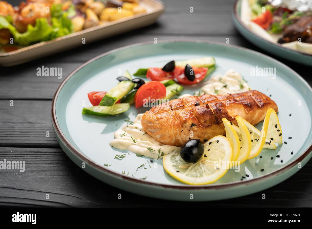 Gegrilltes Lachsfilet serviert mit cremiger Sauce, frischem Gemüse und Zitronenscheiben auf Teller im Restaurant, Meeresfrüchte-Rezept für das Restaurant-Menü pro Person Stockfoto