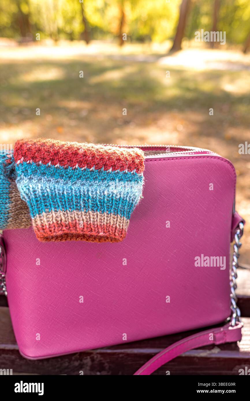 Eine gestreifte Stricksocke ragt aus einer stylischen Damenhandtasche hervor. Wollsocken. Exklusive handgestrickte Artikel. Warme hausgemachte Kleidung. Natürliche Materialien Stockfoto