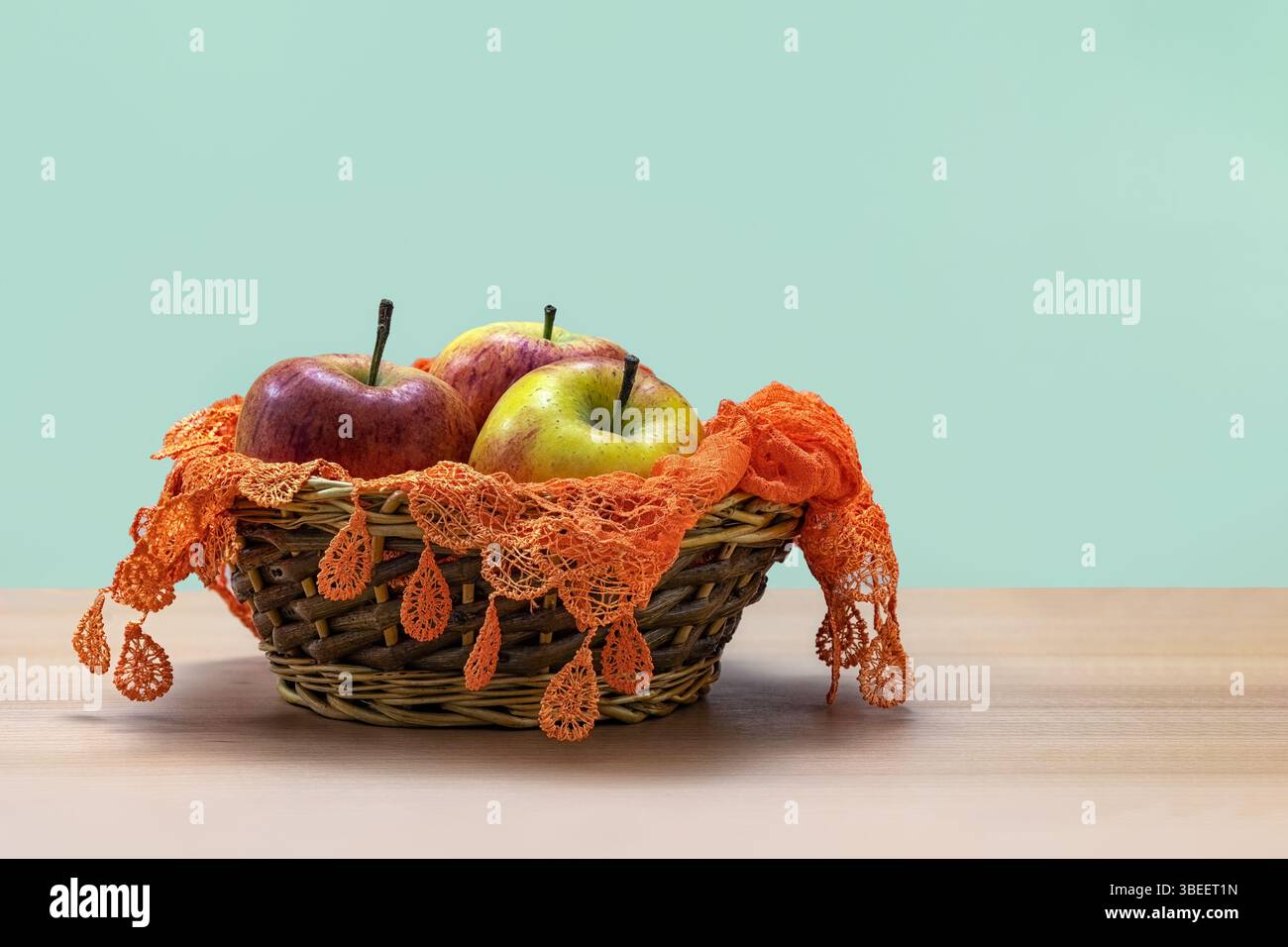 Stillleben reifer Äpfel in einem Korb auf einem Tisch mit orangefarbener Spitze mit hellgrünem Hintergrund Stockfoto