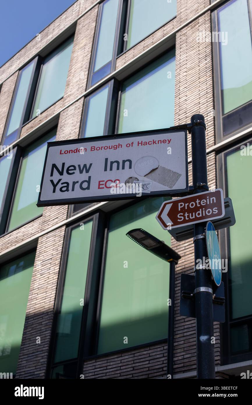 Straßenschilder, einschließlich New Inn Yard, vor einem modernen Gebäude in Hackney, London. Die Schilder zeigen in Richtung Protein Studios. Stockfoto