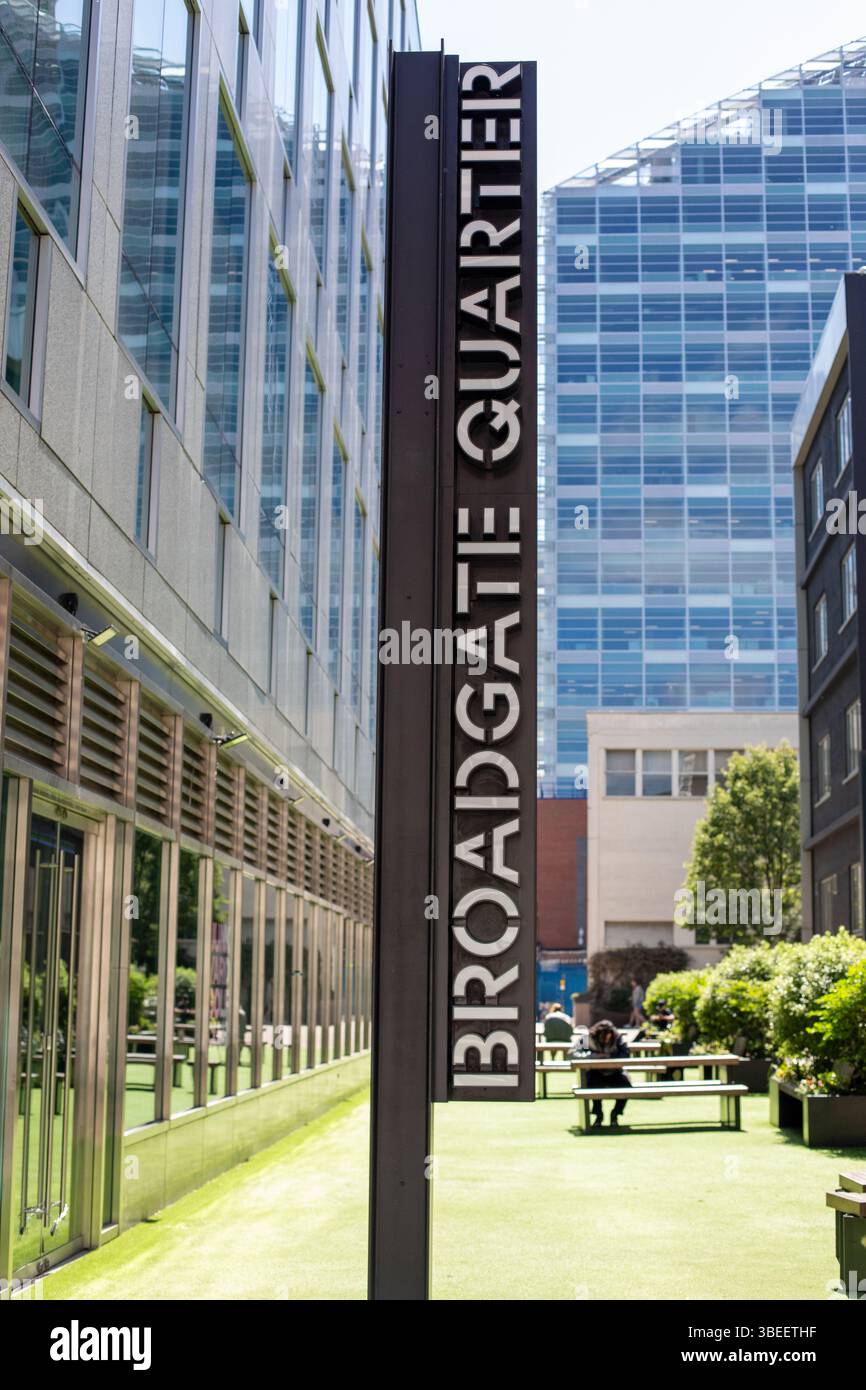 Das Broadgate Quarter-Schild in London steht vor moderner Architektur. Der Bereich verfügt über Grünflächen und Sitzplätze im Freien. Stockfoto