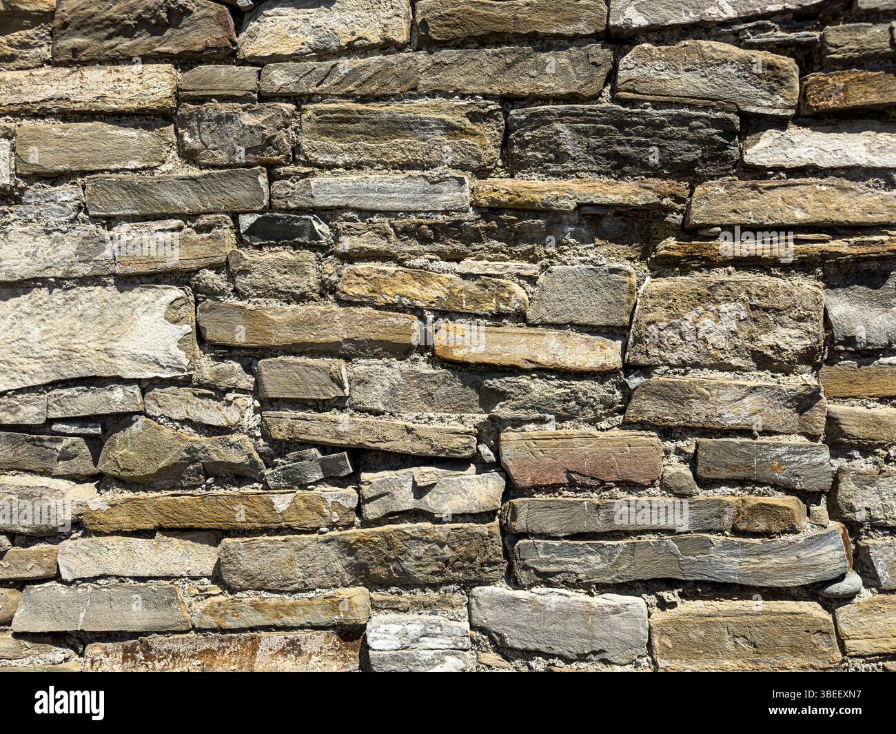 Nahaufnahme der alten Trockensteinmauer mit geschichteten flachen Felsen, rauer Textur und natürlichen Erdtönen, Tageslicht, rustikaler abstrakter Hintergrund. Keine Personen. Stockfoto