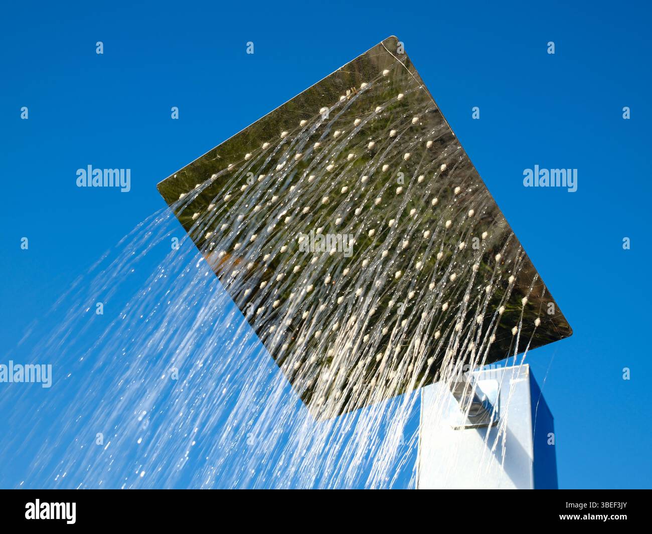 Großer quadratischer Regenduschkopf mit Wasser, das gegen den hellblauen Himmel fällt Stockfoto