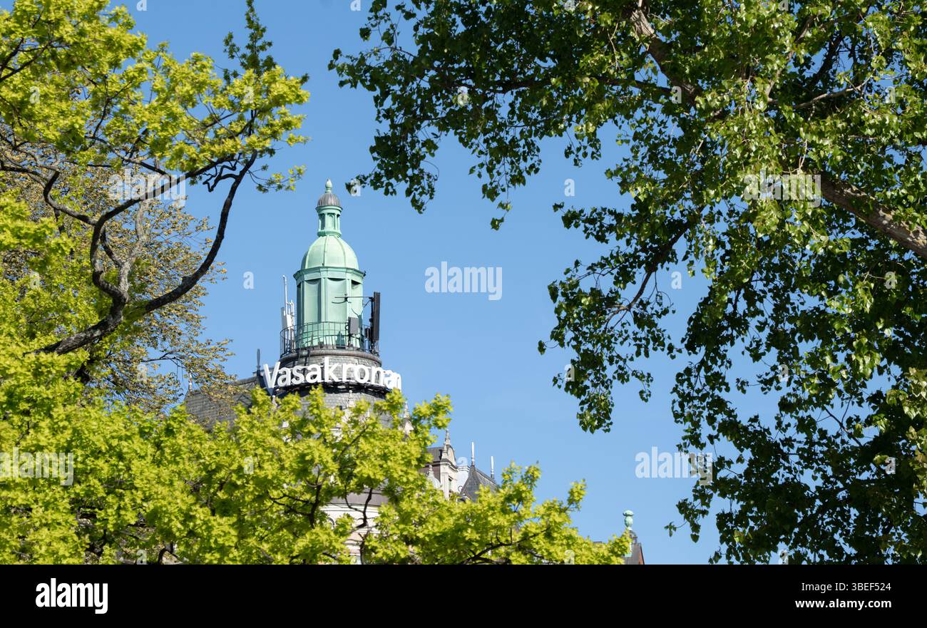 Logo von Vasakronan Fastigheter, einem großen schwedischen Gewerbeimmobilienunternehmen, auf einem Turm aus einem alten Bürogebäude im Stockholmer CBD hinter grünen Bäumen Stockfoto