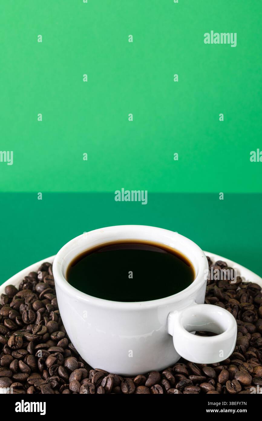 Stilvolles Werbefoto mit einer weißen Keramikschale gefüllt mit schwarzem Kaffee, umgeben von gerösteten Kaffeebohnen. Stockfoto