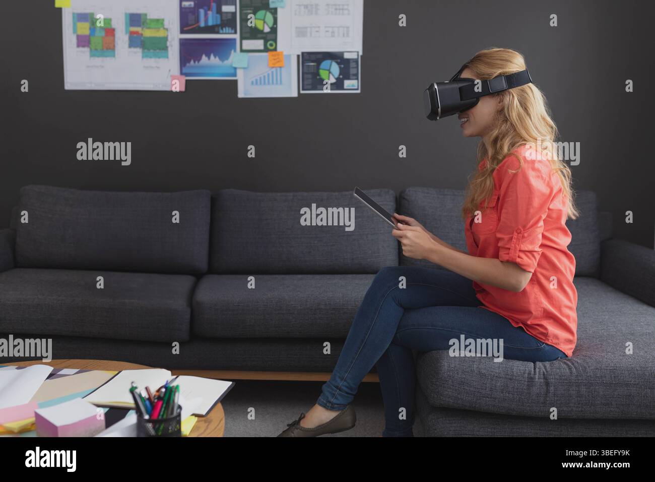 Das Virtual Reality-Headset liegt auf einem Tablet auf einem hölzernen Couchtisch mit verstreuten Papieren und Diagrammen Stockfoto