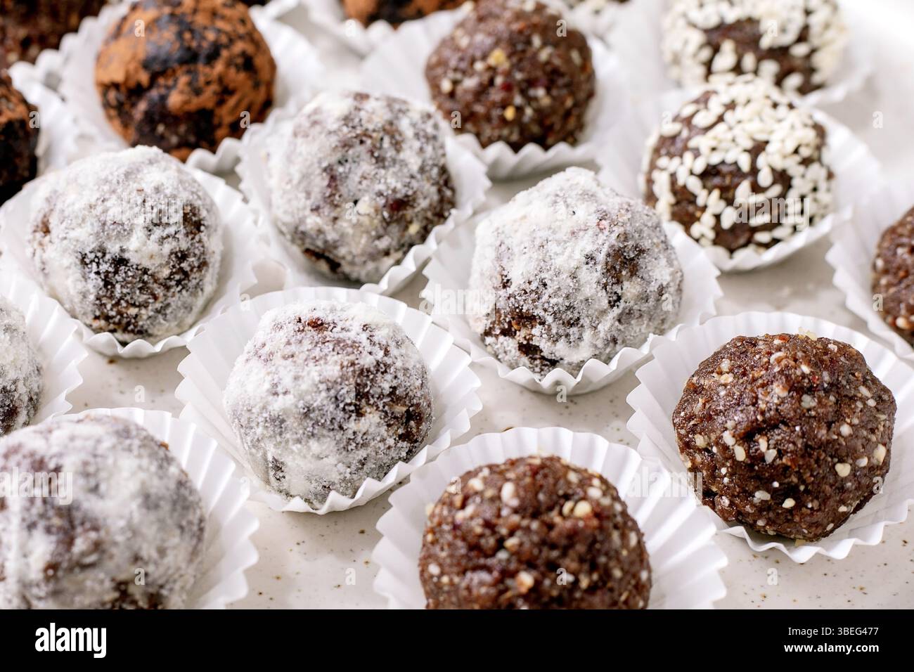 Hausgemachte Schokoladentrüffel rohe vegane Kugeln weiße Pappbecher. Zu den verschiedenen Beschichtungen gehören Puderzucker-Kakaonüsse. Süßes Gourmet-Dessert. Stockfoto