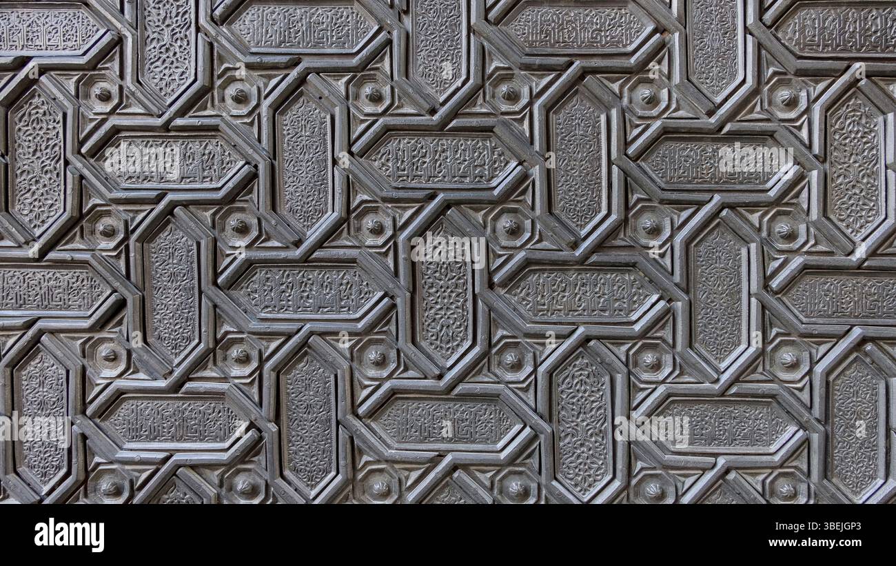 Kunstvolles islamisches geometrisches Muster, das in eine Metalloberfläche geschnitzt wurde, zeigt komplizierte Handwerkskunst und detaillierte kalligraphische Inschriften, wiederholtes Design Stockfoto