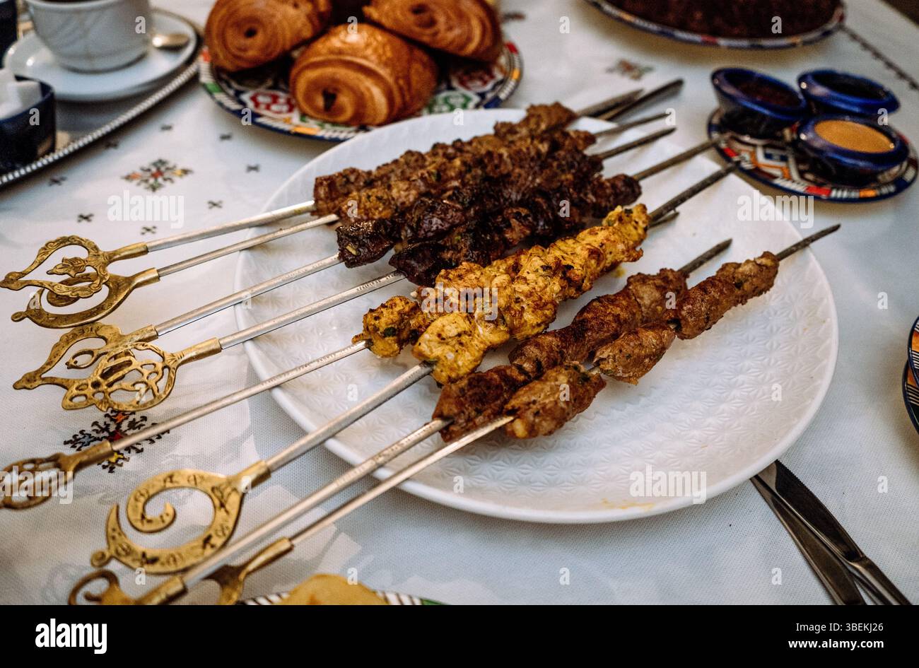 Verschiedene gegrillte Fleischspieße auf traditionellem Tisch mit dekorativen Tellern Mai 29,2025 Stockfoto
