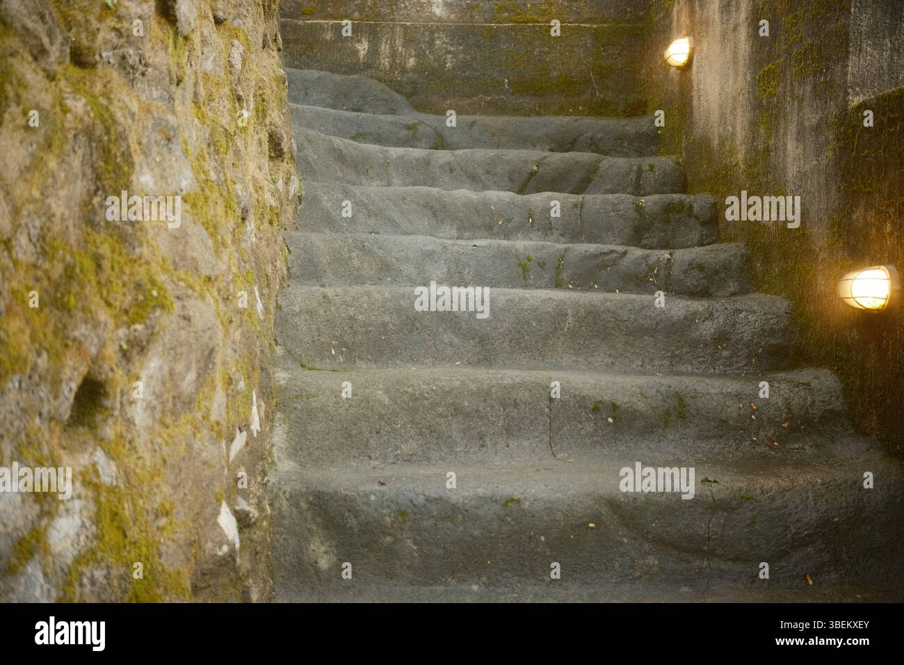 Eine alte Steintreppe, flankiert von moosbedeckten Wänden und kleinen Wandlampen Stockfoto