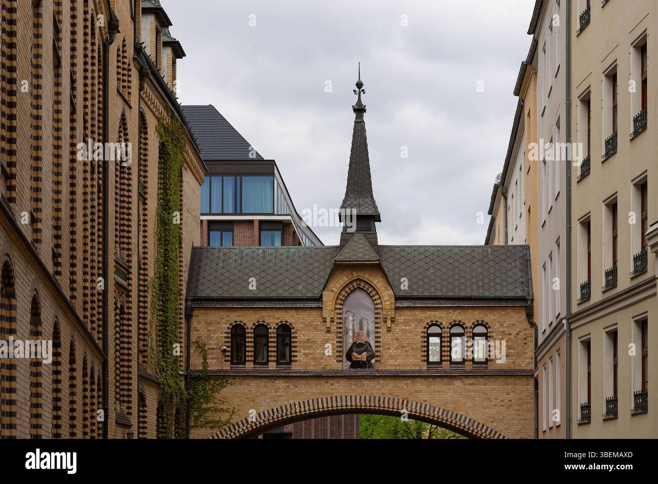 Historische Fußgängerbrücke mit Bogenfenstern und einem spitzen Turm, der zwei klassische Backsteinhäuser in der europäischen Stadt verbindet Stockfoto