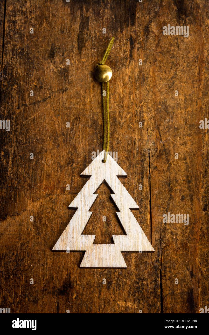 Eine handgefertigte Dekoration in Form eines Tannenbaums wird von einer grünen Schnur an einer strukturierten Holzoberfläche aufgehängt. Stockfoto