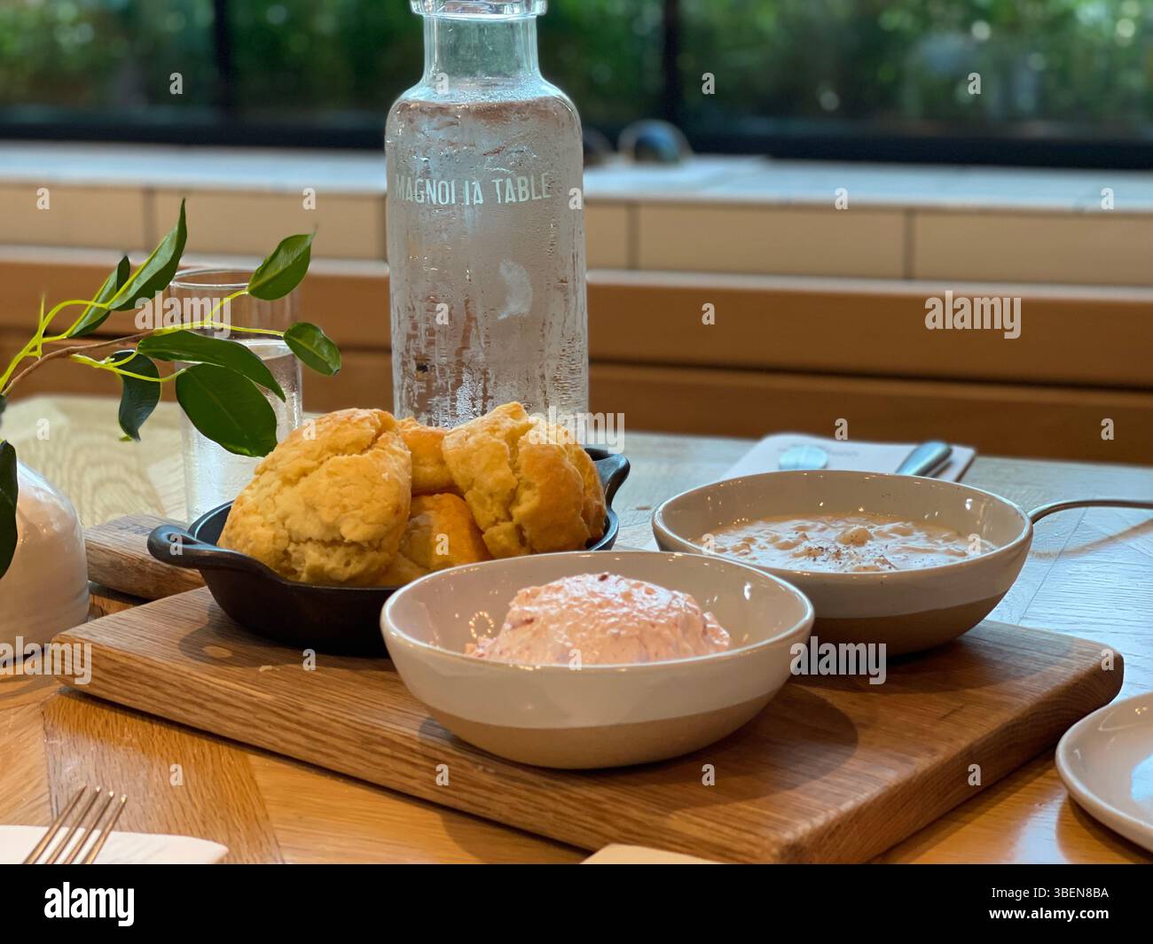 Frisch gebackene Kekse serviert mit cremiger Suppe und verteilt auf einem Holztablett mit einer klaren Wasserflasche auf einem rustikalen Holztisch. - Smartphone-aufgenommenes Stockfoto
