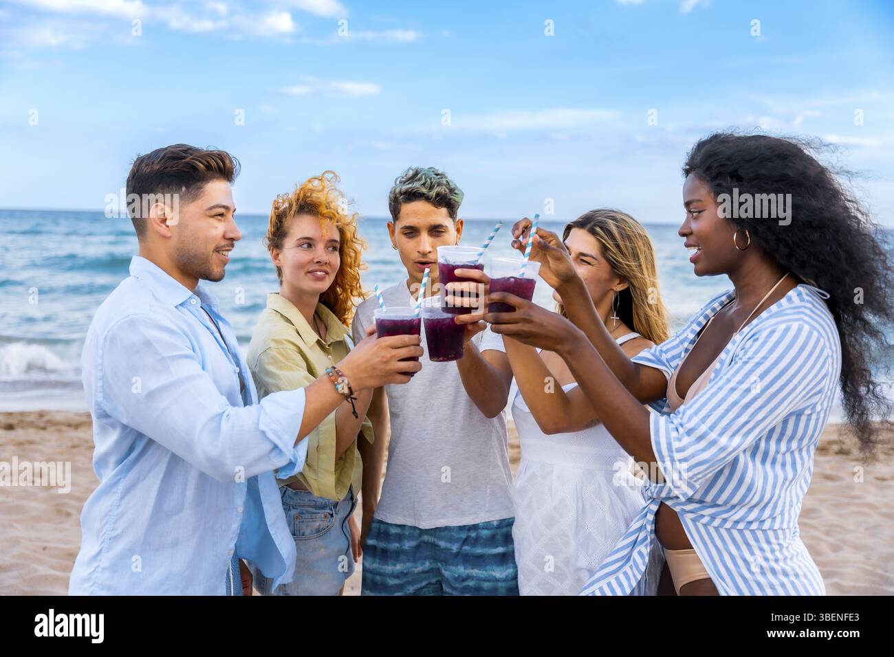Gruppe von verschiedenen Freunden, die erfrischende Getränke teilten und gemeinsam unter der hellen Sonne an einem wunderschönen Strand an einem schönen Strand rösten, um Freundschaft und Freude zu feiern Stockfoto