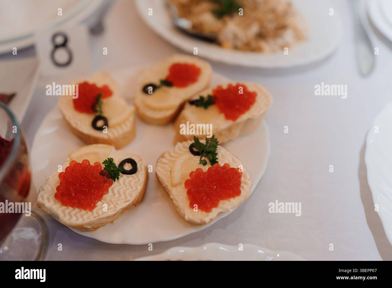 Elegante Häppchen mit rotem Kaviar und Kräutern, präsentiert auf weißen Tellern an einem formellen Tisch, mit delikaten Backwaren und luxuriösen Speisen Stockfoto