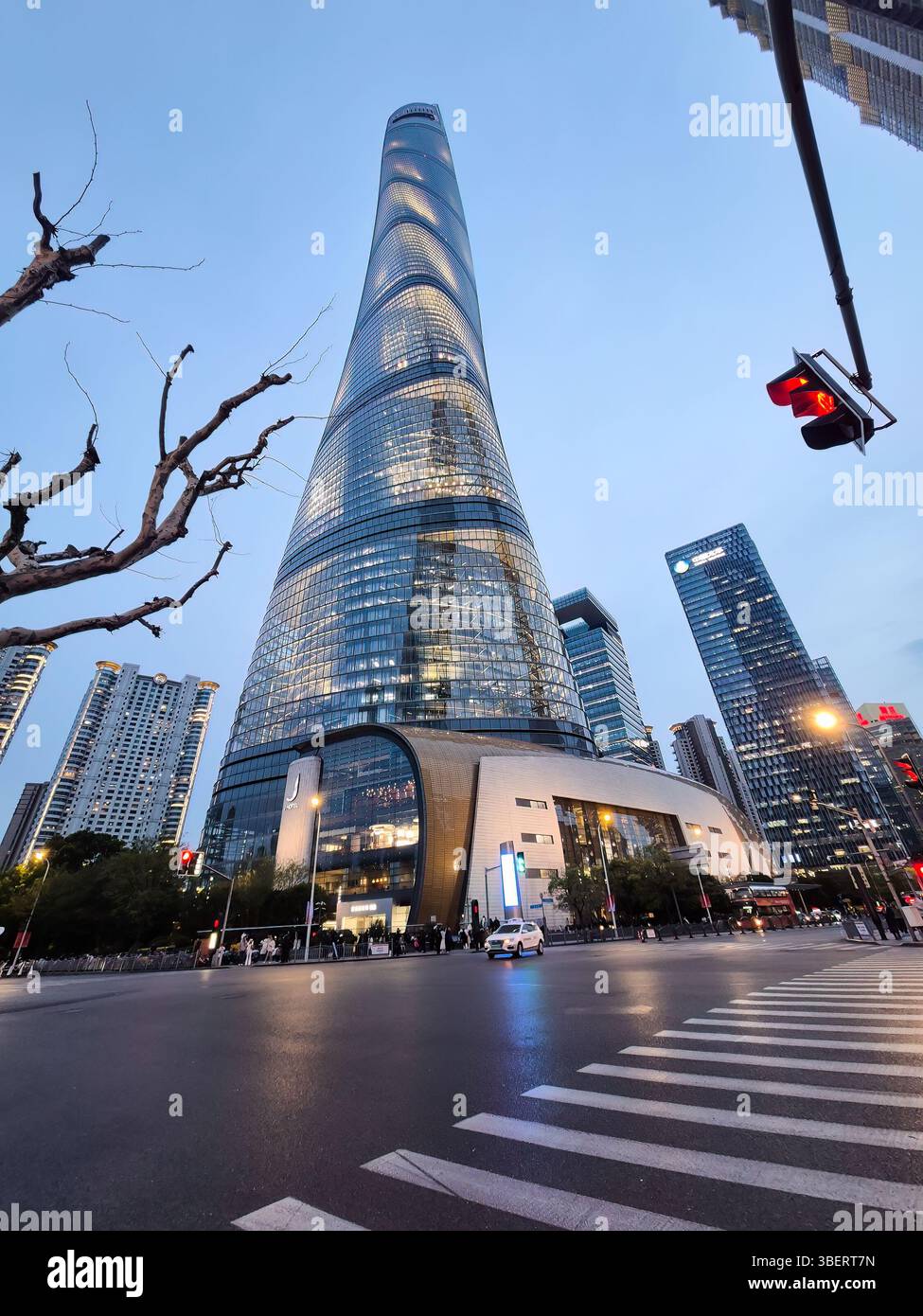 Shanghai, China - 1. April 2025: Blick auf den Shanghai Tower in der Abenddämmerung, umgeben von modernen Wolkenkratzern und Stadtleben an einer geschäftigen Kreuzung in der Innenstadt. Stockfoto