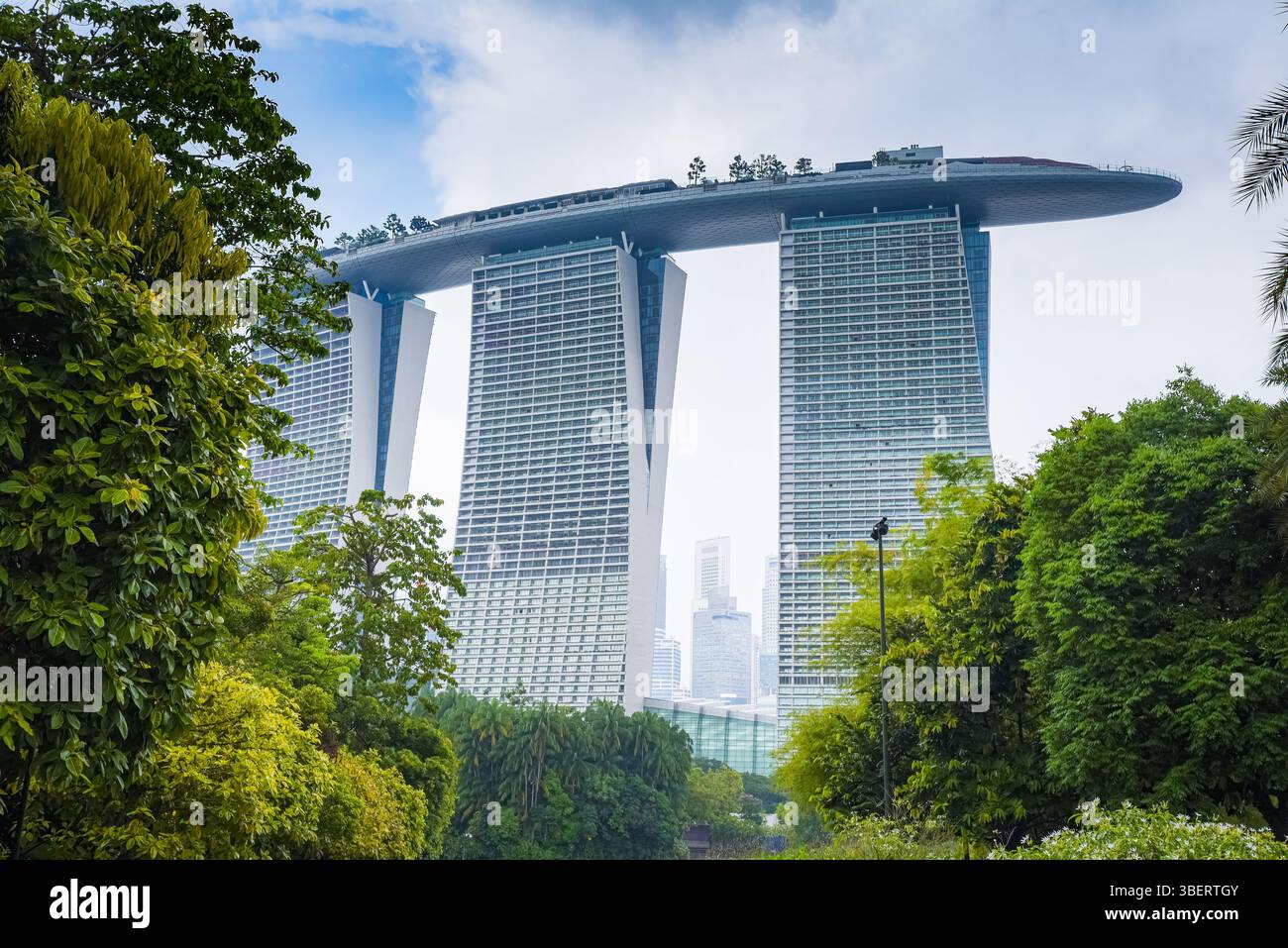 Singapur, Singapur – 4. April 2025: Blick auf das ikonische Marina Bay Sands Hotel, umgeben von tropischem Grün, mit seinem Sky Park, der sich über drei erstreckt Stockfoto