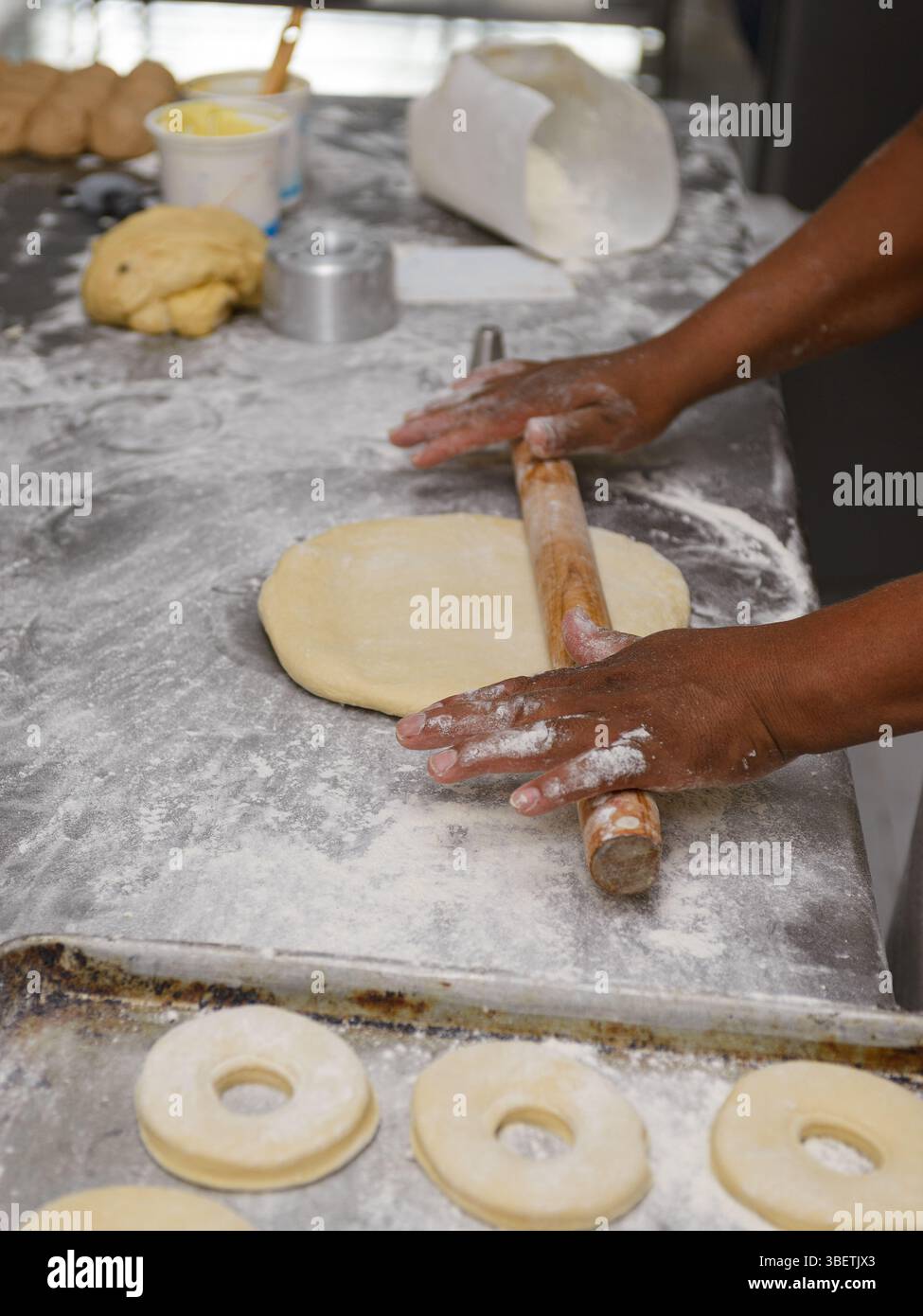 Männliche Hände Rollen den Teig geschickt auf einer bemehlten Oberfläche aus und bereiten ihn für die Ringringe vor. Stockfoto