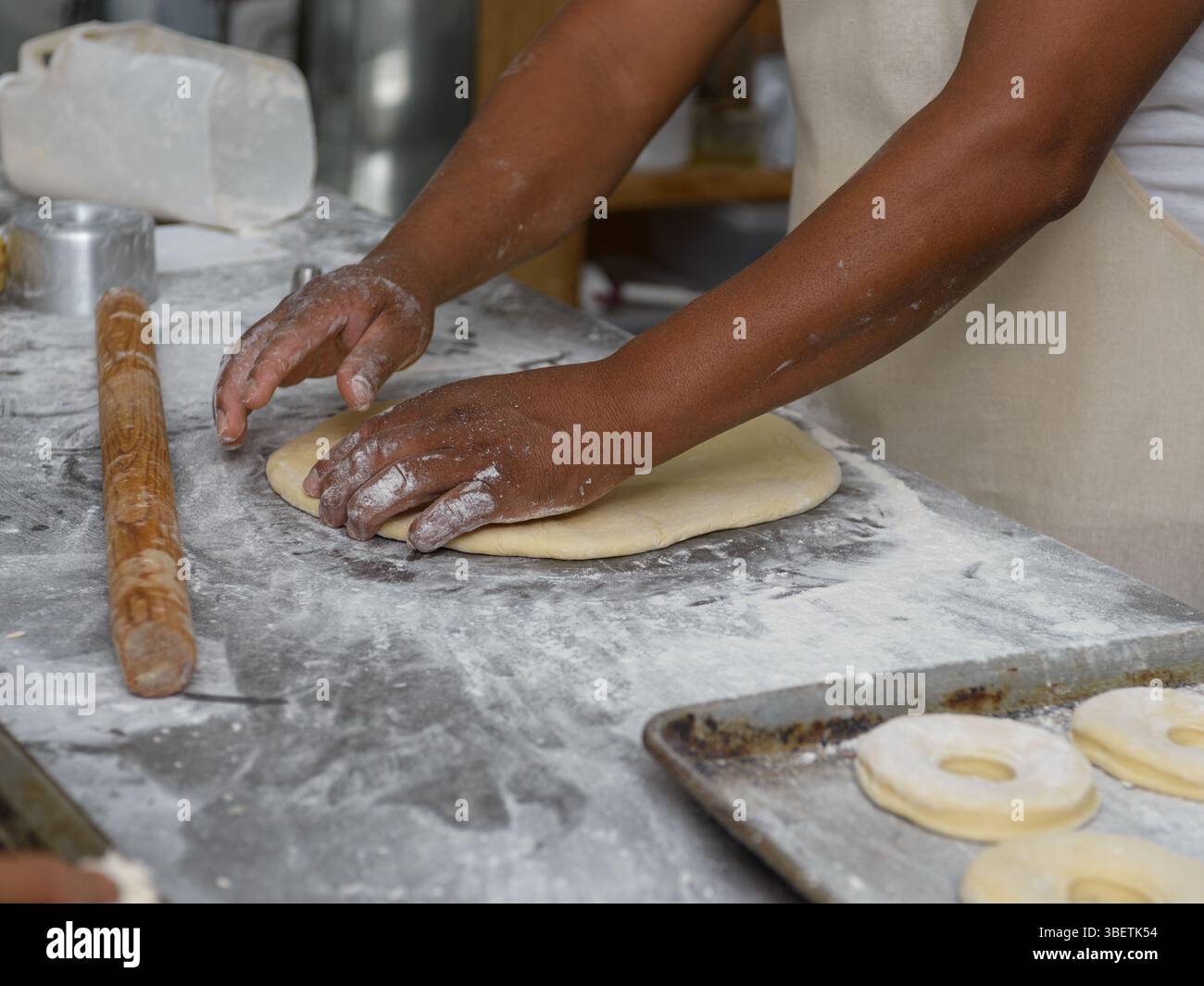 Männliche Hände Rollen den Teig geschickt auf einer bemehlten Oberfläche aus und bereiten ihn für die Ringringe vor. Stockfoto