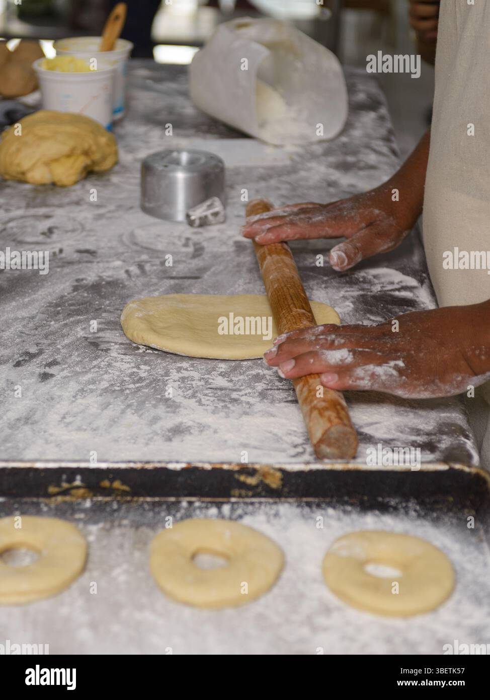 Männliche Hände Rollen den Teig geschickt auf einer bemehlten Oberfläche aus und bereiten ihn für die Ringringe vor. Stockfoto