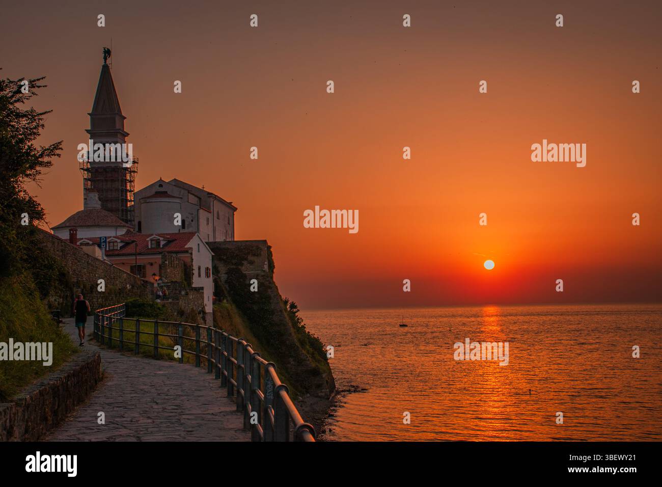 Die Stadt Piran leuchtet bei Sonnenuntergang, ihre warmen Farben spiegeln sich auf der ruhigen Adria wider und verbinden Architektur, Meer und Himmel in perfekter Harmonie. Stockfoto