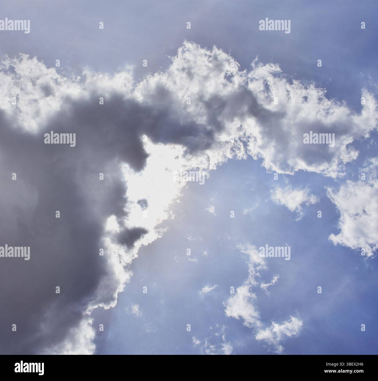 Sonnenstrahlen, die durch Wolkenbedeckung an einem klaren Himmel auftauchen. Aufmunternde und ruhige Tagesszene. Stockfoto