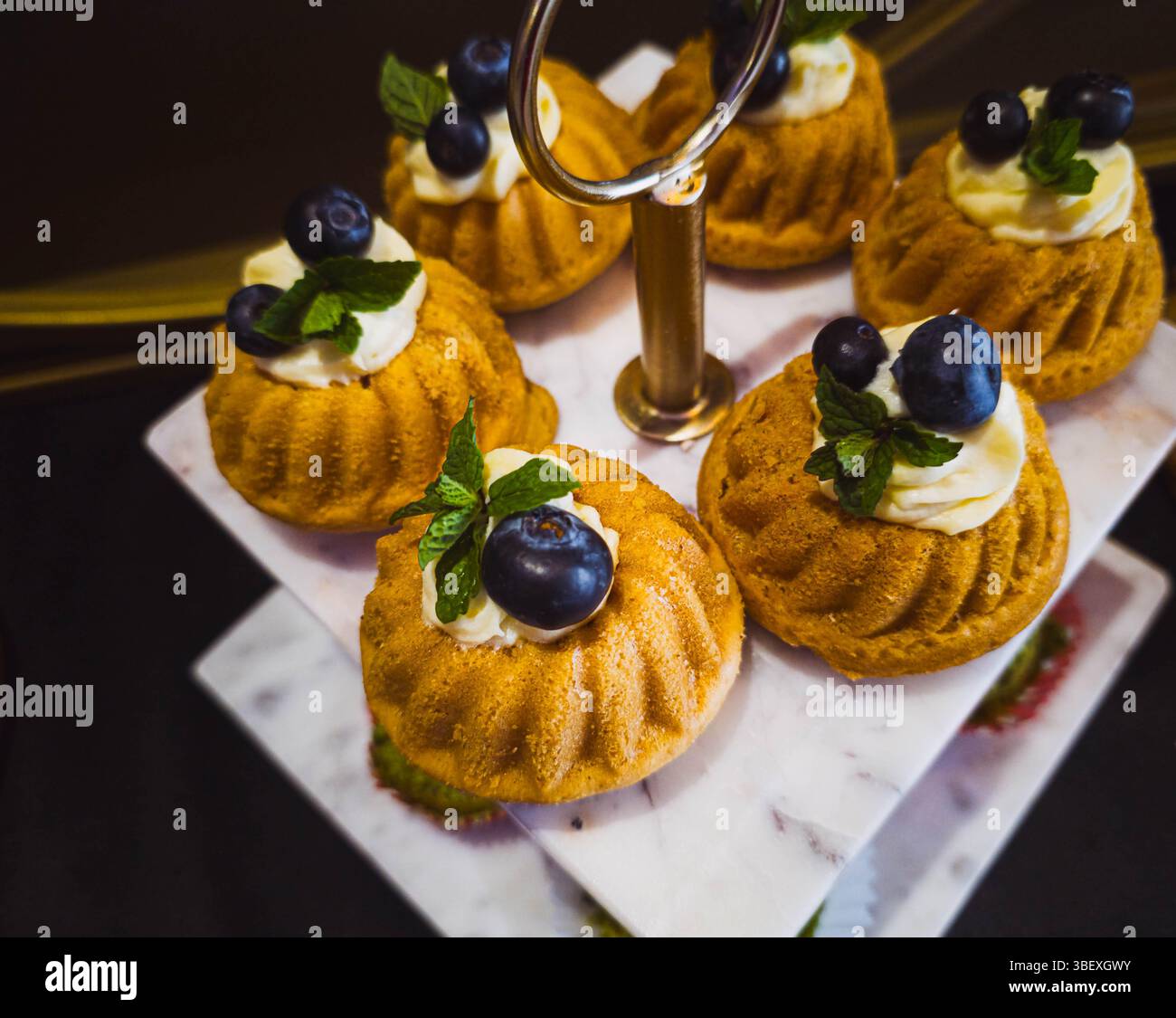 Mini-Bundt-Kuchen mit Heidelbeeren und Creme auf Marmorständer. - Smartphone-aufgenommenes Stockfoto